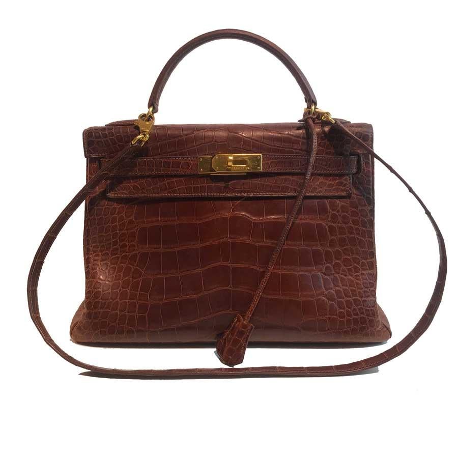 Kelly from Maison Hermès in size 32 cm, it is in a mat brown alligator and its jewelry is in gold metal. It has its shoulder strap measuring 90 cm, more for carrying on the shoulder than cross body. This kelly bag has its alligator bell with the two