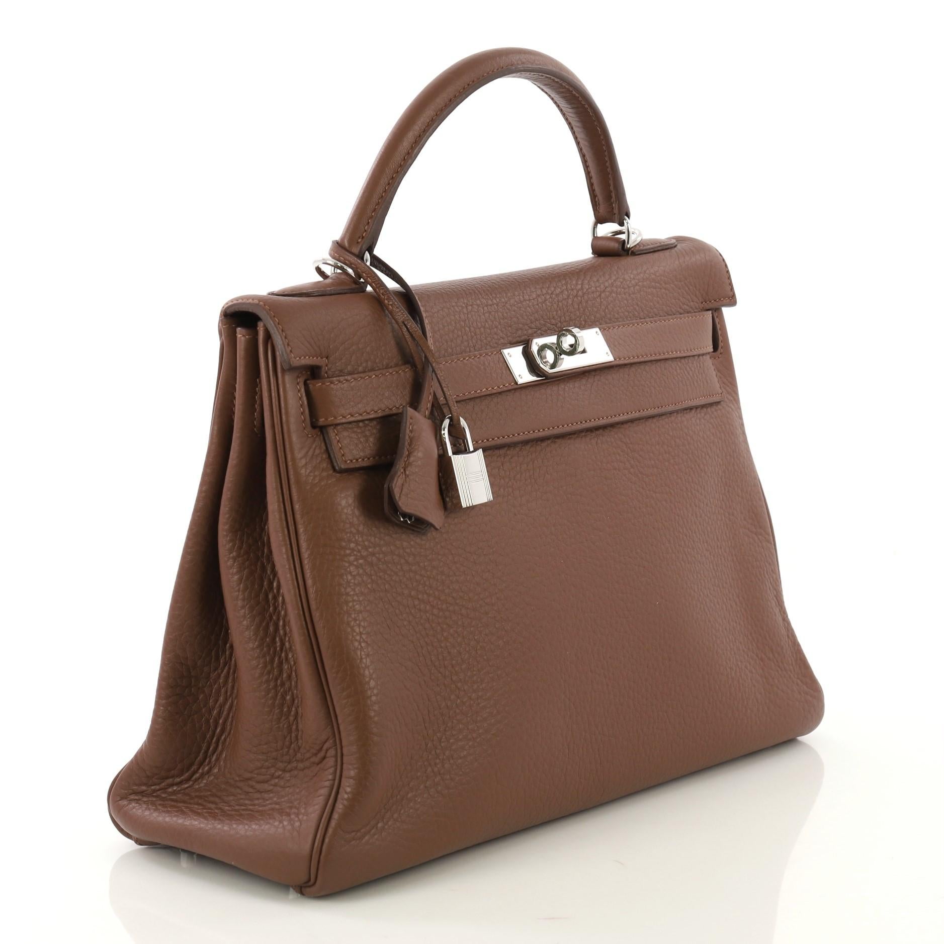 This Hermes Kelly Amazone Handbag Marron d'Inde Clemence with Palladium Hardware 32, crafted in Marron d'Inde brown Clemence leather, features a single rolled top handle, protective base studs, and palladium hardware. Its turn-lock closure opens to