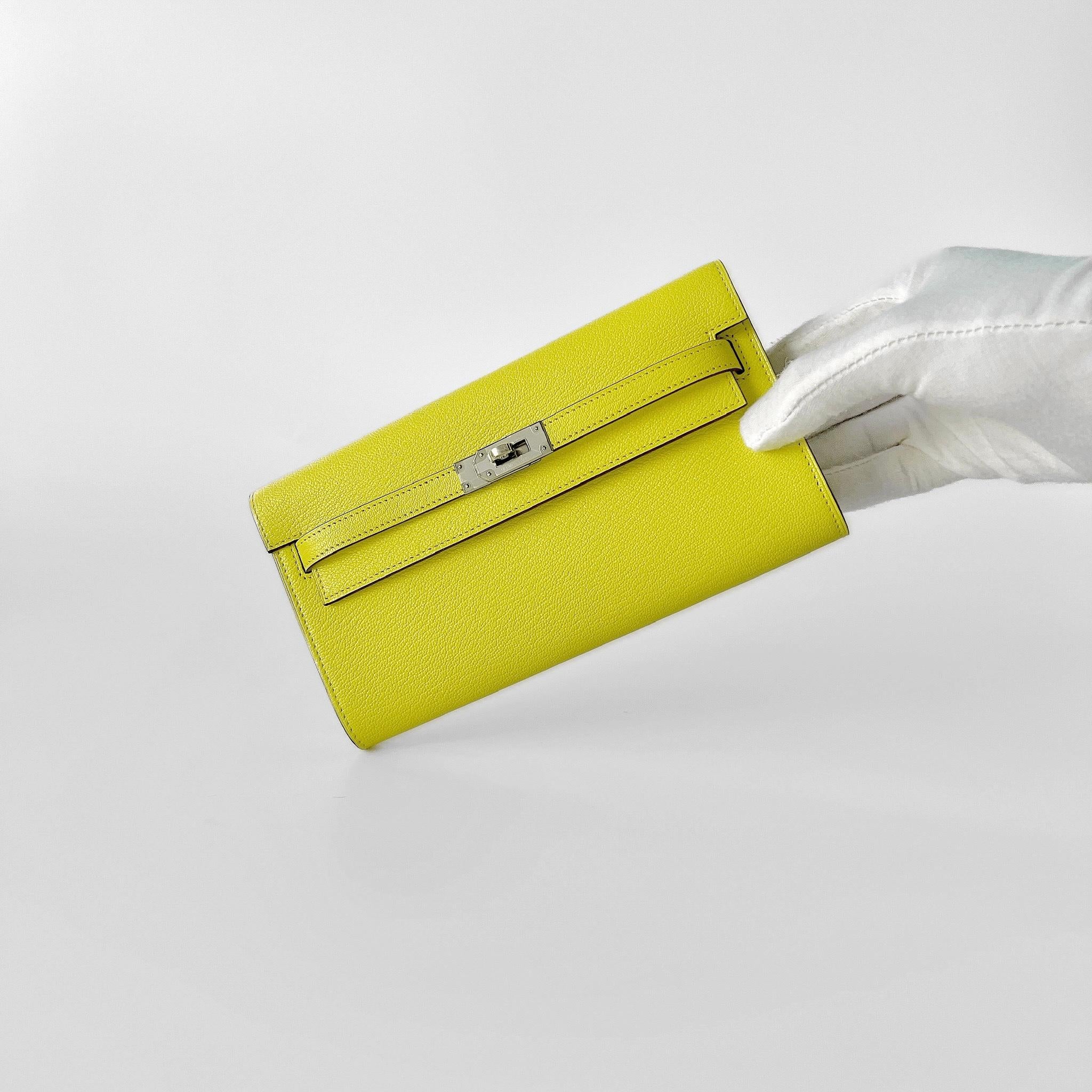 Shop this eye catching Hermes Kelly Classique To Go Wallet, In Jaune Citron With Palladium Hardware. It is crafted in Epsom Leather and comes with a strap which makes the wallet usable as both a clutch and a bag. There are 4 credit card slots and a