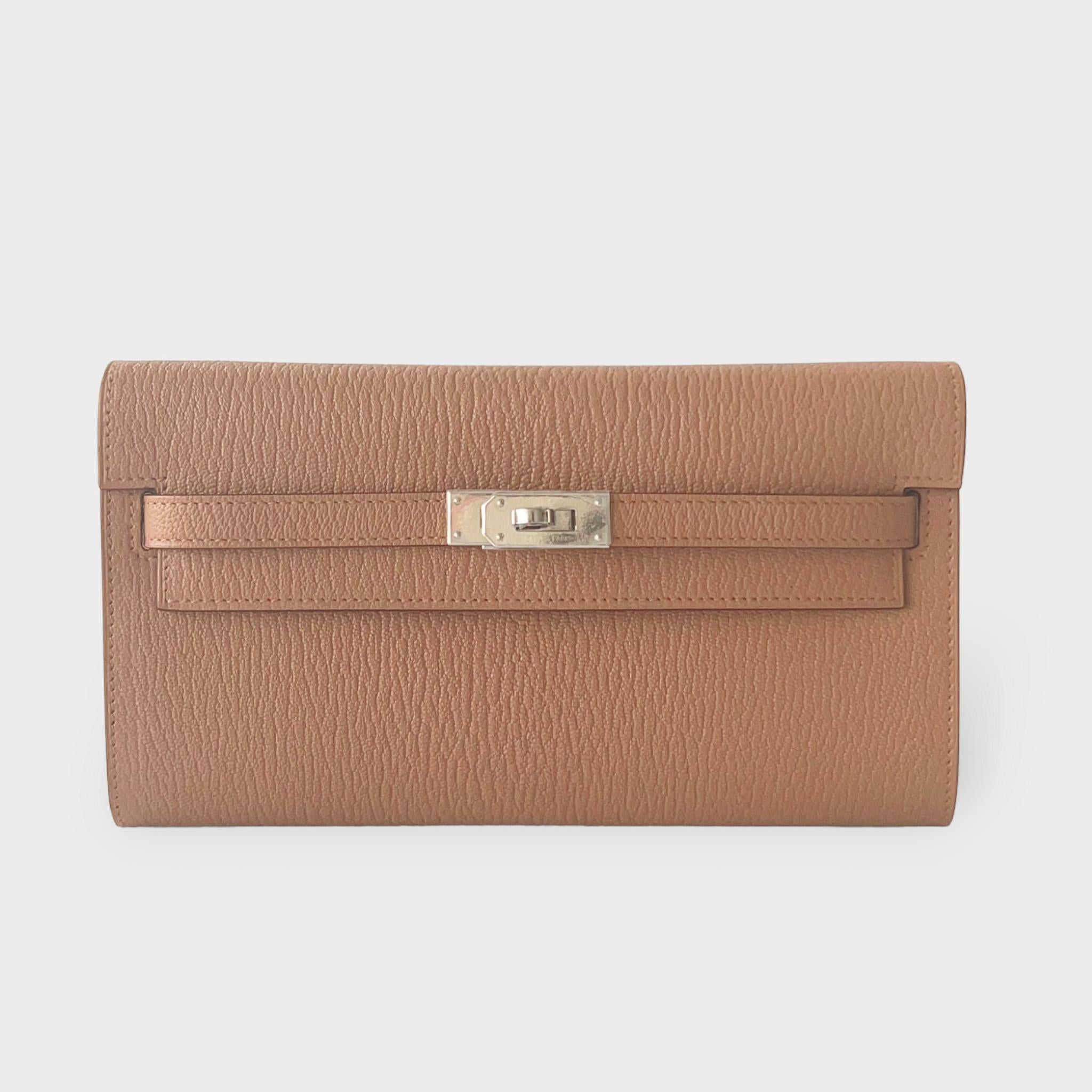 Shop this eye catching Hermes Kelly Classique To Go Wallet, In Quebracho, a light brown that is complimented with Palladium Hardware. It is crafted in Mysore Goatskin Leather and comes with a strap which makes the wallet usable as both a clutch and