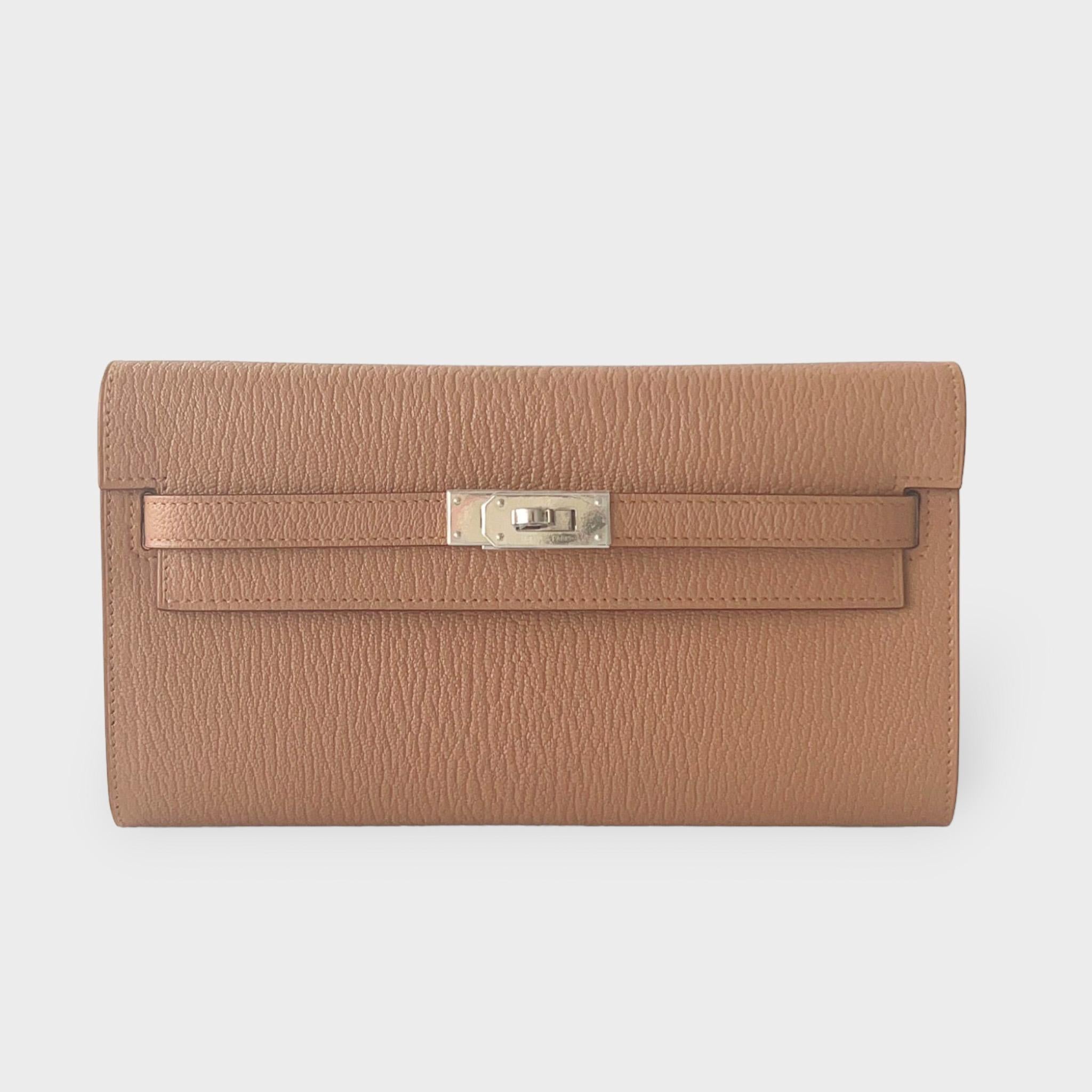 Shoppen Sie diese auffällige Hermes Kelly Classique To Go Geldbörse in Quebracho, einem hellen Braun, das mit Palladium-Hardware ergänzt wird. Sie ist aus Mysore-Ziegenleder gefertigt und wird mit einem Riemen geliefert, der das Portemonnaie sowohl