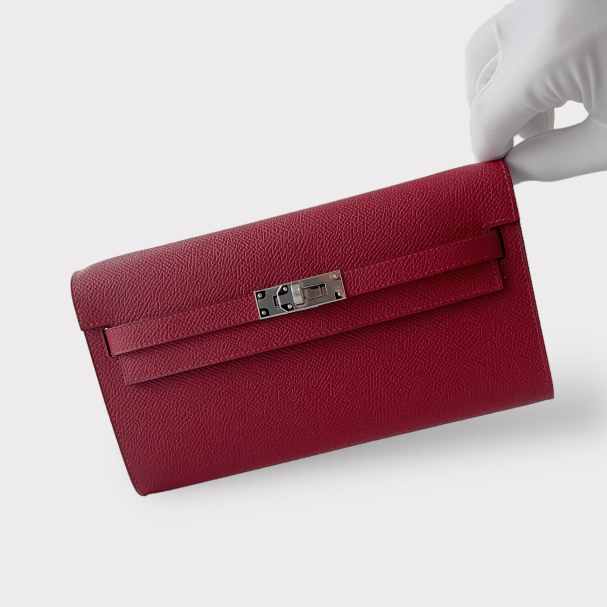 Shop this eye catching Hermes Kelly Classique To Go Wallet, In Red, Rouge Grenat With Palladium Hardware. It is crafted in Epsom Leather and comes with a strap which makes the wallet usable as both a clutch and a bag. There are 4 credit card slots
