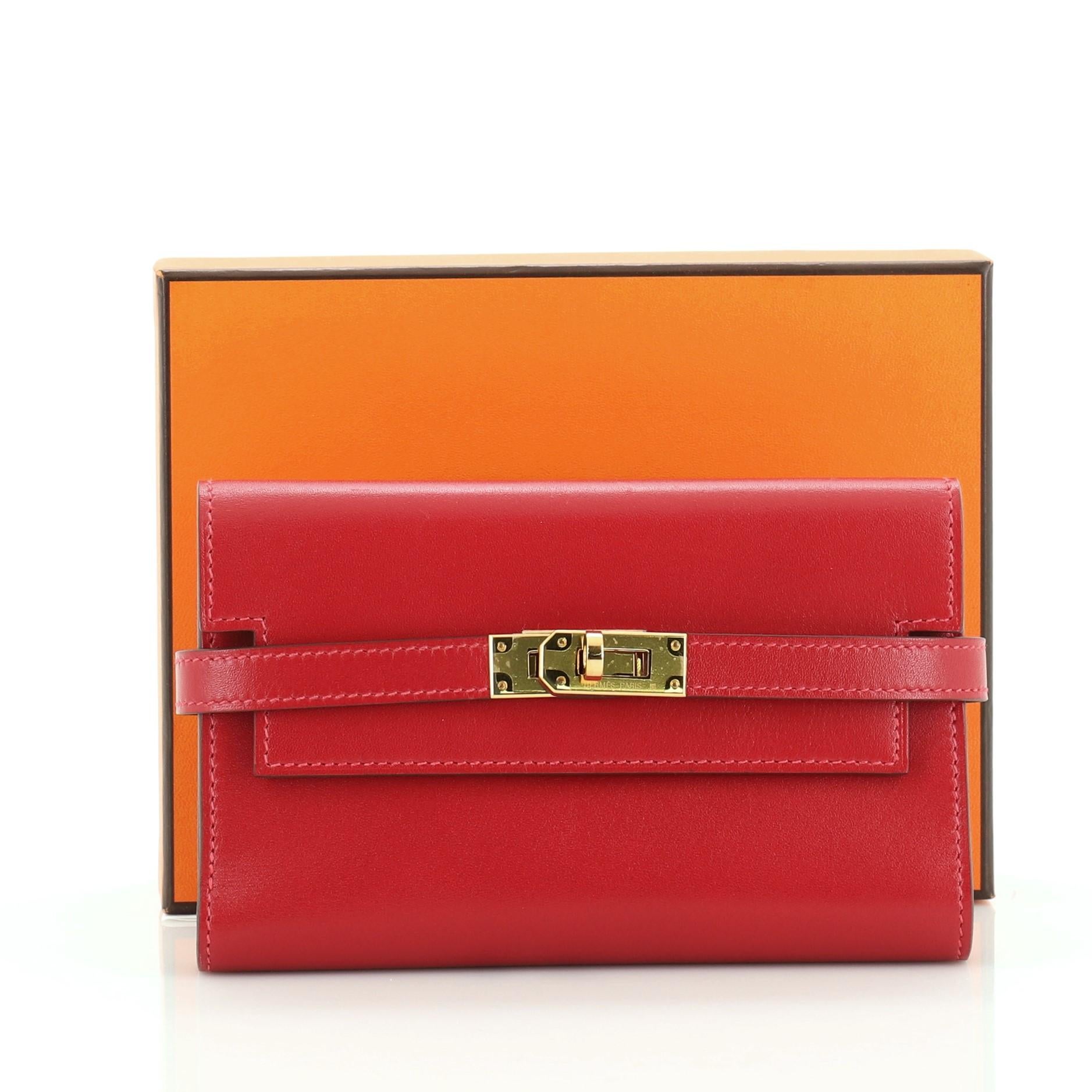 This Hermes Kelly Depliant Wallet Tadelakt Medium, crafted in Rouge Vif red Tadelakt leather, features its iconic turn-lock closure, subtle Hermes logo at its center and gold hardware. It opens to a Rouge Vif red Tadelakt leather with a middle