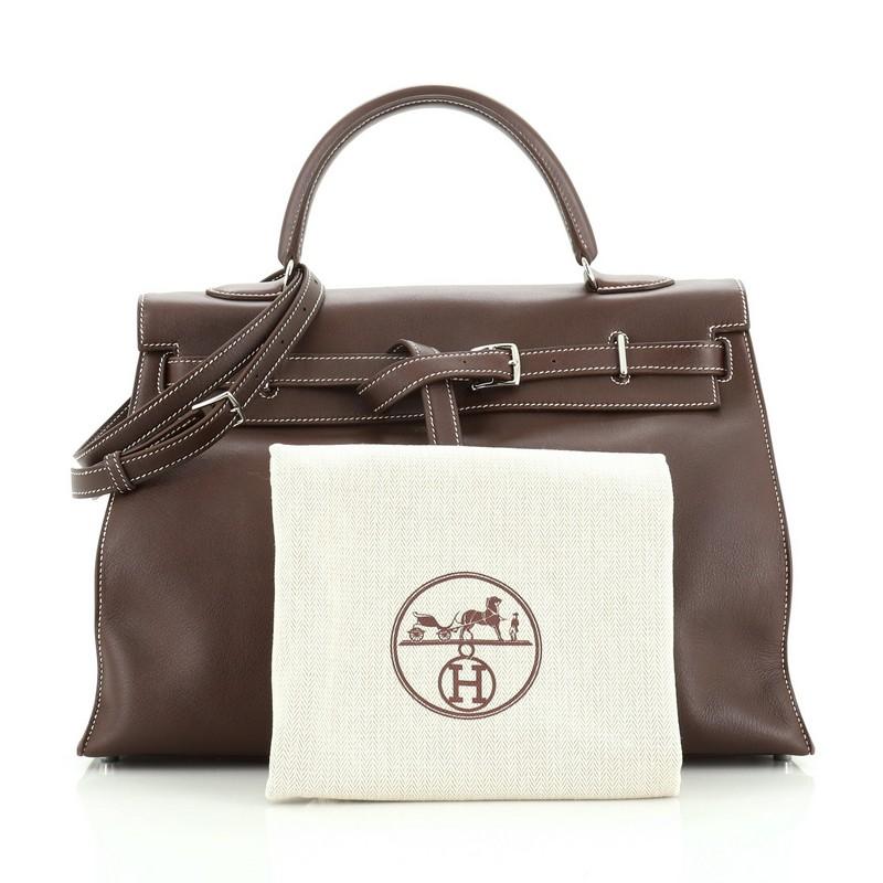 This Hermes Kelly Flat Handbag Havane Swift with Palladium Hardware 35, crafted in Havane brown swift leather, features single rolled top handle, unique Hermes etriviere belt strap closure and palladium-tone hardware. Its flap opens to a Havane