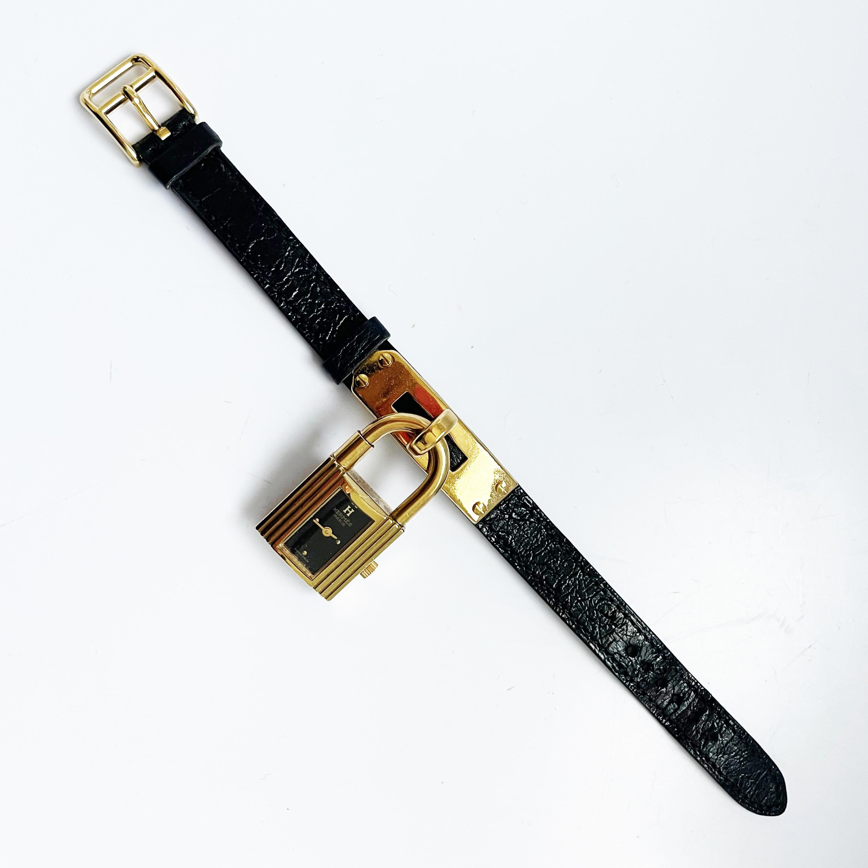 Authentic, preowned, vintage 90s Hermes Kelly cadena watch in gold metal with a black Chèvre Mysore leather strap.  Stamped T in a circle, indicating a 1990 year of production.  Iconic style with black watch face and Swiss movement.  

Remove the