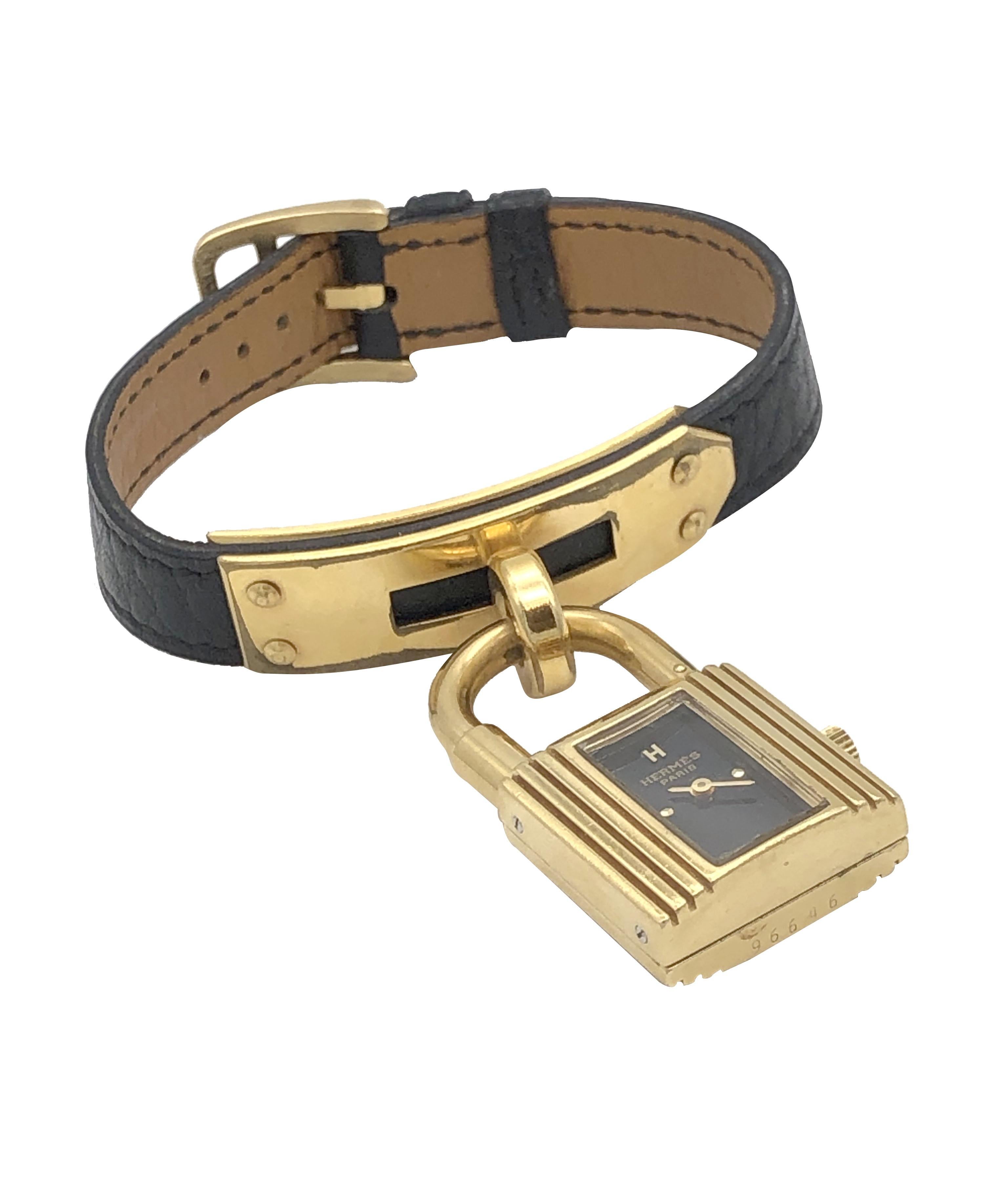 Circa 2000 Hermes Kelly collection Ladies Wrist watch, 1 7/8 inch  X  3/4 inch Gold tone Lock form watch, Quartz movement, Black dial, Black Leather strap with tang buckle, watch length 7 1/4 inches and is adjustable.