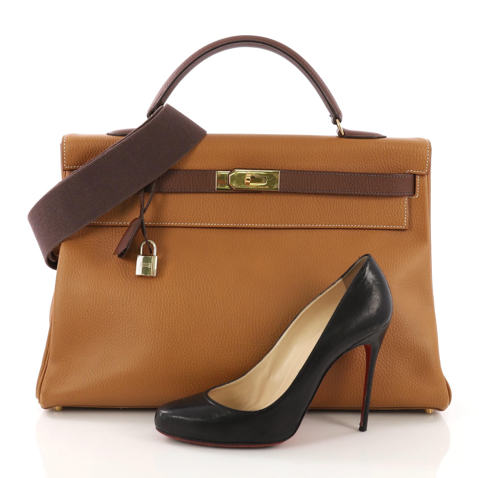 This Hermes Kelly Handbag Bicolor Ardennes with Gold Hardware 40, crafted in Natural and Marron Fonce Ardennes leather, features a single rolled top handle, frontal flap, and gold hardware. Its turn-lock closure opens to a Natural brown Chevre