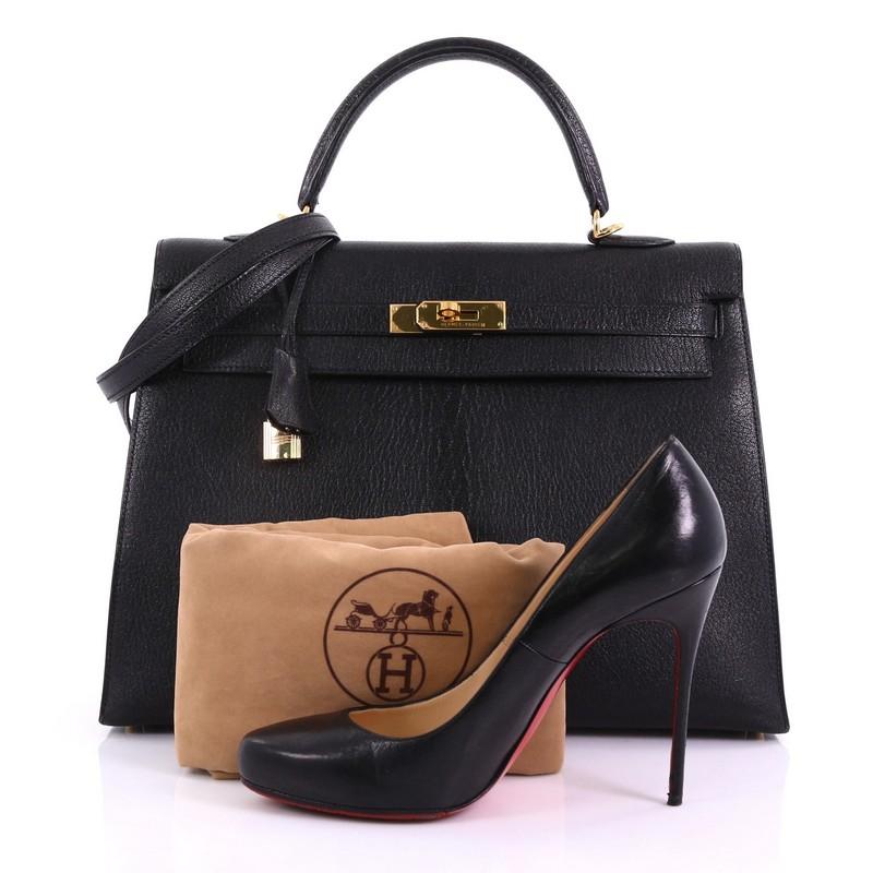This Hermes Kelly Handbag Black Chevre de Coromandel with Gold Hardware 35, crafted in Noir black Chevre de Coromandel, features a single rolled top handle, protective base studs, and gold-tone hardware. Its turn-lock closure opens to a black