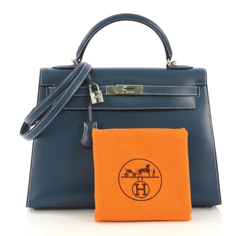 This Hermes Kelly Handbag Bleu Thalassa Box Calf with Palladium Hardware 32, crafted in Blue Tempete blue Box Calf leather, features a single rolled top handle, frontal flap, and palladium hardware. Its turn-lock closure opens to a Blue Tempete blue