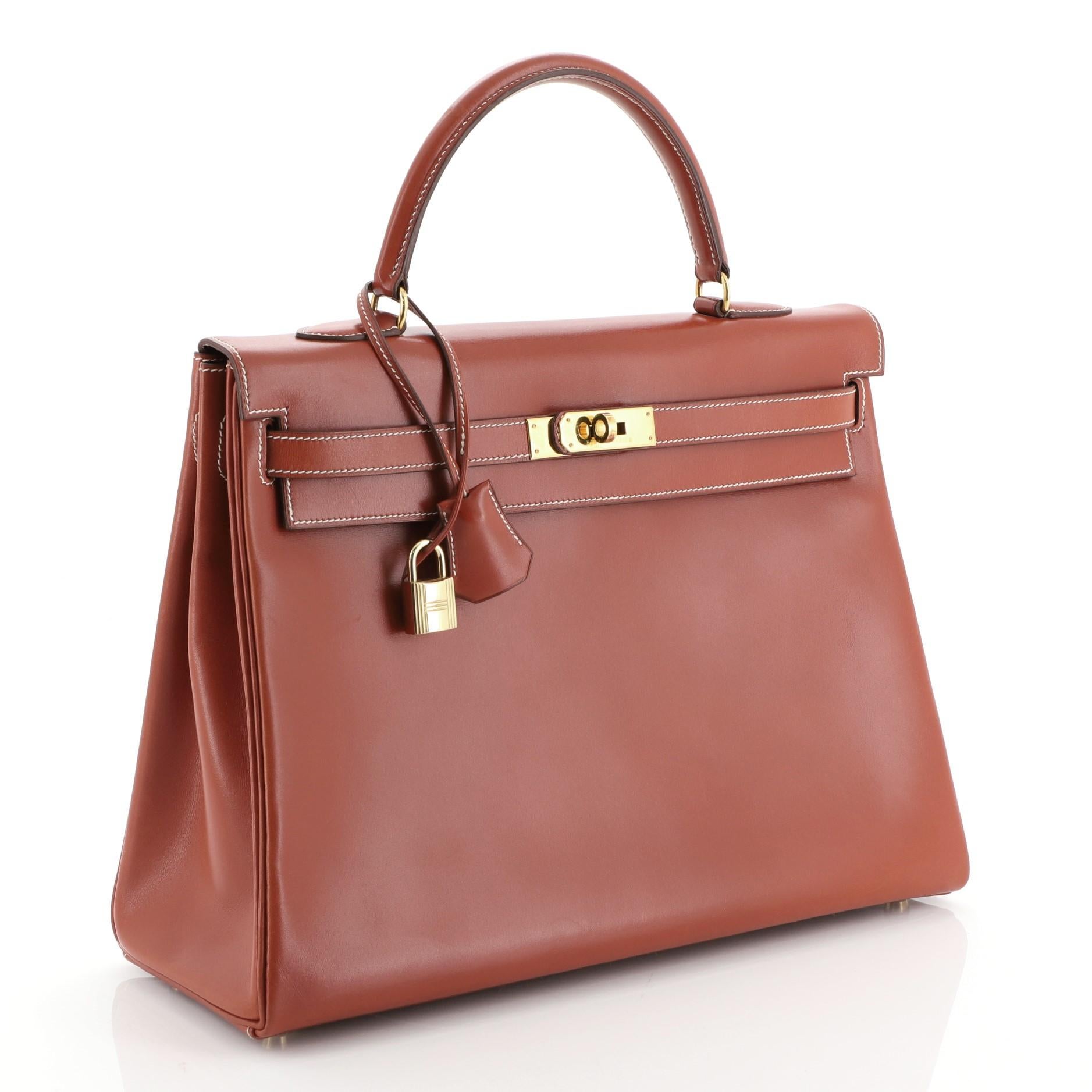 This Hermes Kelly Handbag Brique Box Calf with Gold Hardware 35, crafted in Brique orange Box Calf leather, features a single top handle, protective base studs, and gold hardware. Its turn-lock closure opens to a Brique orange Chevre leather