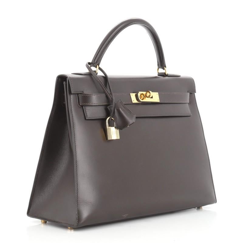 This Hermes Kelly Handbag Chocolate Box Calf with Gold Hardware 32, crafted from Chocolate brown Box Calf leather, features a single top handle and gold hardware. Its turn-lock closure opens to a Chocolate brown Chevre leather interior with zip and