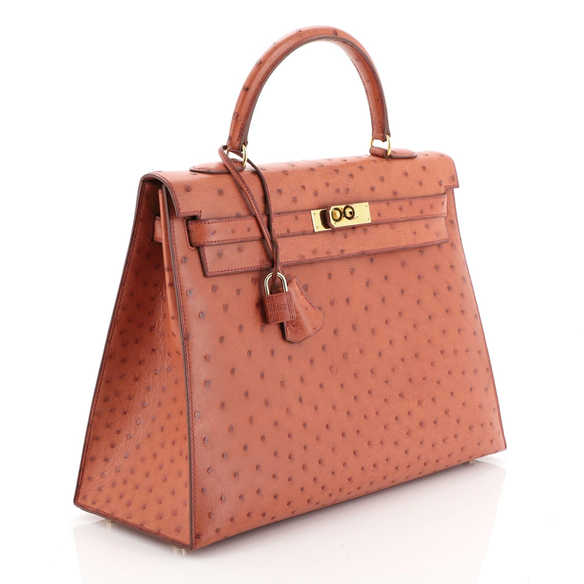 This Hermes Kelly Handbag Cognac Ostrich with Gold Hardware 35, crafted in genuine Cognac orange ostrich, features a single rolled top handle, protective base studs, and gold hardware. Its turn-lock closure opens to a Cognac orange Chevre leather