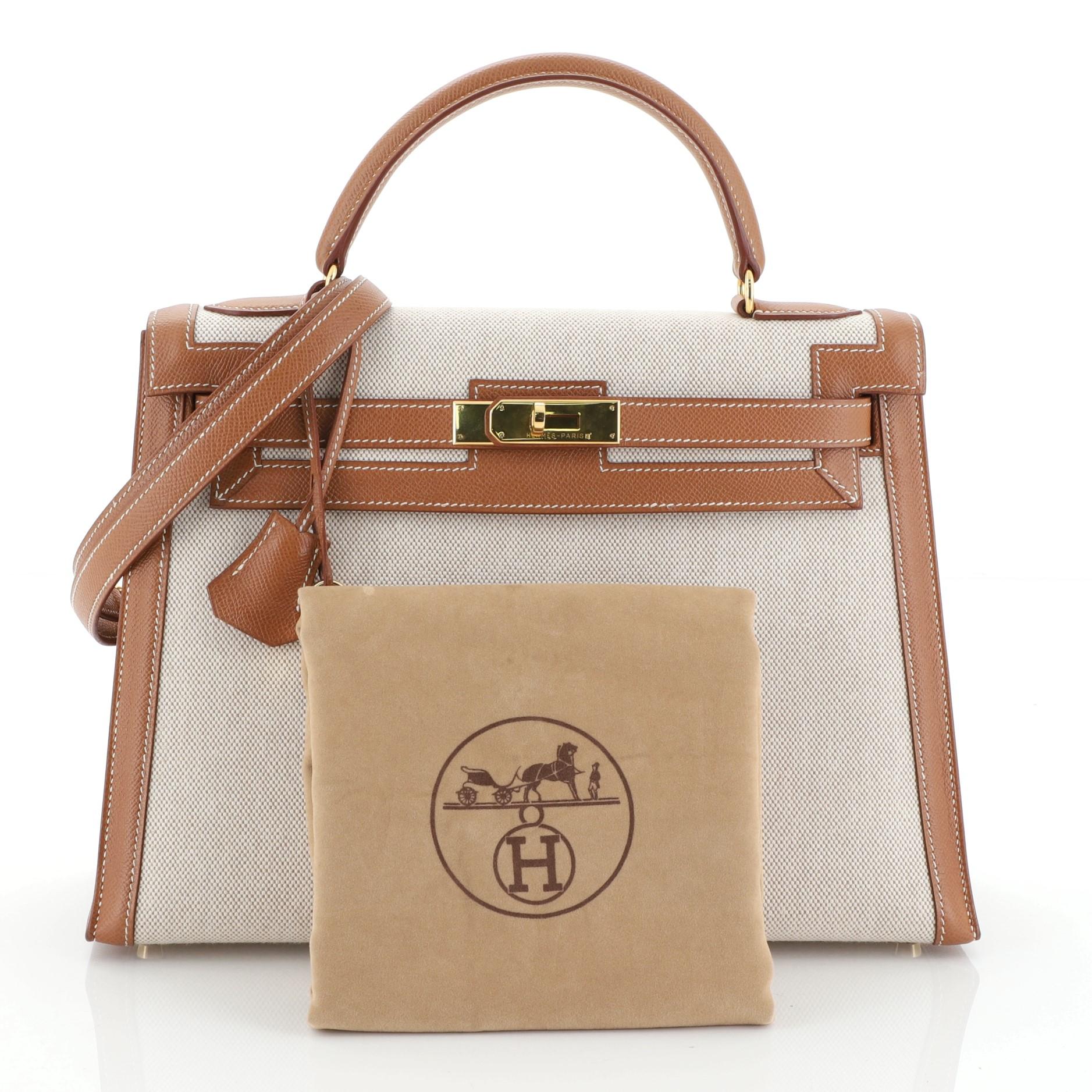 This Hermes Kelly Handbag Ecru Toile and Gold Courchevel with Gold Hardware 32, crafted in Ecru neutral Toile H and Gold brown Courchevel leather, features a single rolled top handle, protective base studs, and gold hardware. Its turn-lock closure