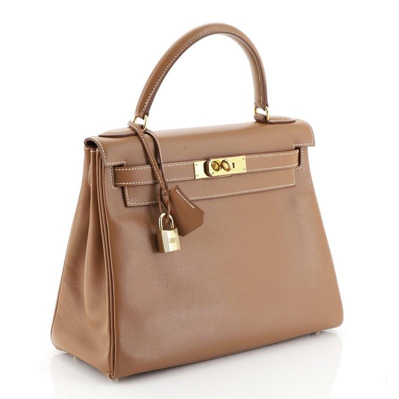 This Hermes Kelly Handbag Gold Courchevel with Gold Hardware 28, crafted from Gold brown Courchevel leather, features a single top handle and gold hardware. Its turn-lock closure opens to a Gold brown Chevre leather interior with zip and slip