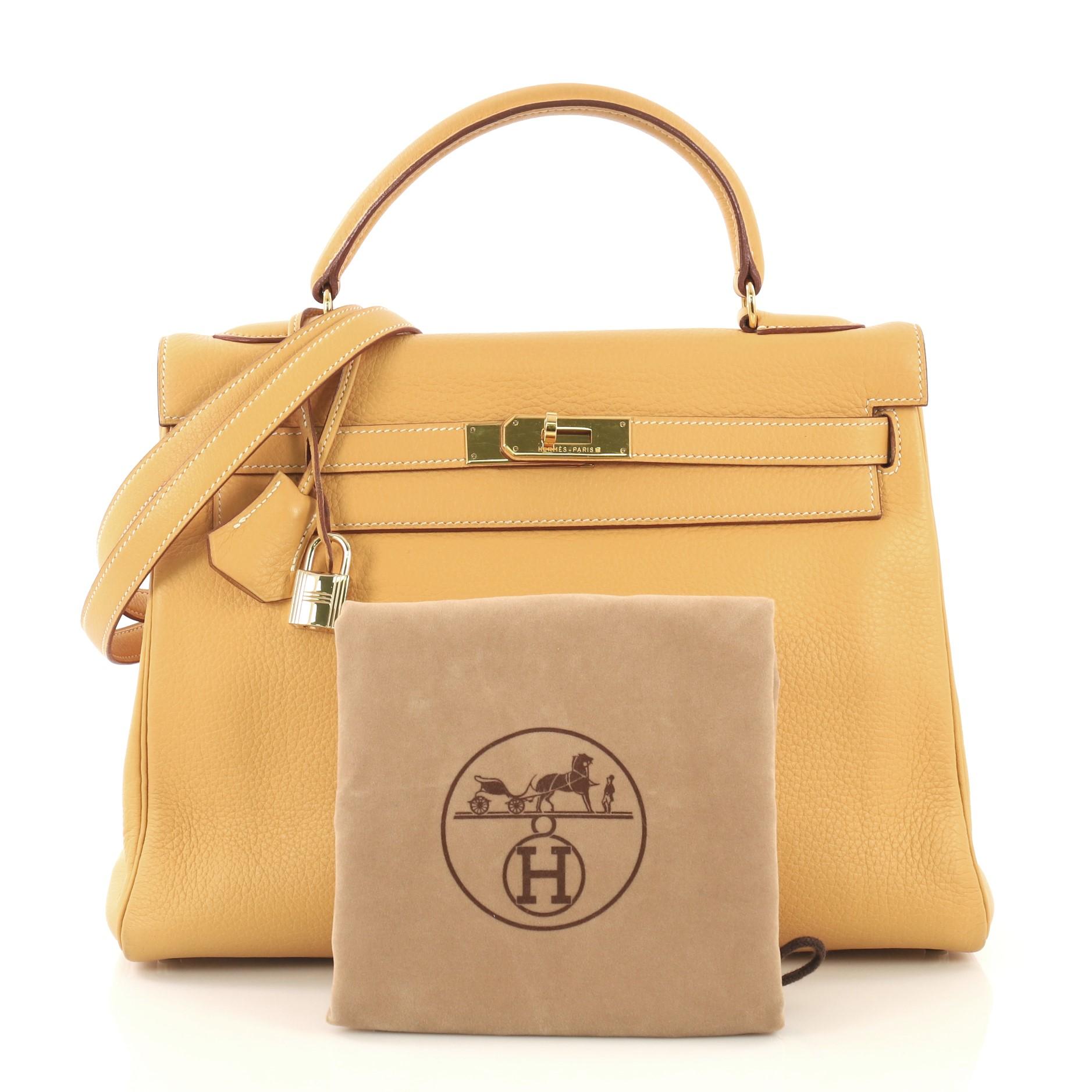 This Hermes Kelly Handbag Natural Sable Clemence with Gold Hardware 32, crafted in Natural Sable yellow Clemence leather, features a single rolled top handle, frontal flap, and gold hardware. Its turn-lock closure opens to a Natural Sable yellow