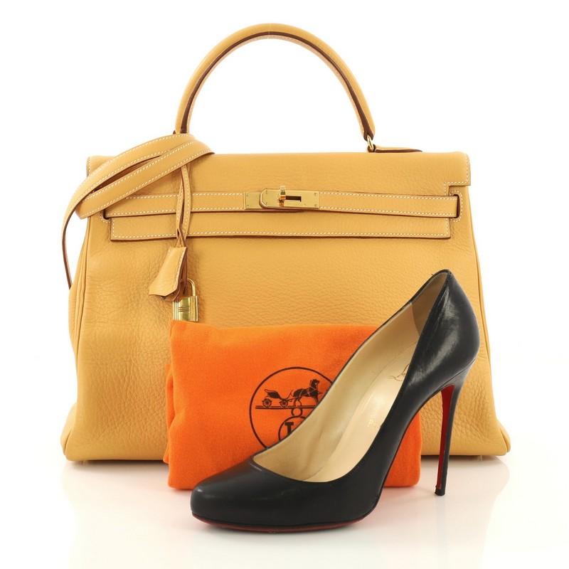 This Hermes Kelly Handbag Natural Sable Clemence with Gold Hardware 35, crafted from Natural Sable yellow Togo leather, features a single rolled top handle, frontal flap, turn lock closure, and gold-tone hardware. It opens to a yellow leather
