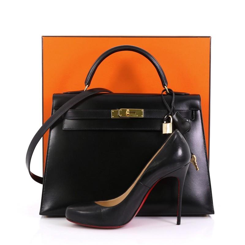 This Hermes Kelly Handbag Noir Box Calf with Gold Hardware 32, crafted from Noir black Box Calf leather, features single looped top handle, frontal flap, and gold hardware. Its turn-lock closure opens to a Noir black Chevre leather interior with zip