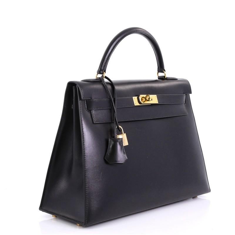 This Hermes Kelly Handbag Noir Box Calf with Gold Hardware 32, crafted in Noir black Box Calf leather, features a single rolled top handle, protective base studs, and gold hardware. Its turn-lock closure opens to a Noir black Chevre leather interior