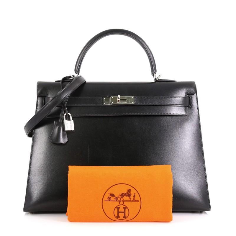 This Hermes Kelly Handbag Noir Box Calf with Palladium Hardware 35, crafted from Noir black Box Calf leather, features a single rolled top handle, frontal flap, protective base studs, and palladium hardware. Its turn-lock closure opens to a Noir