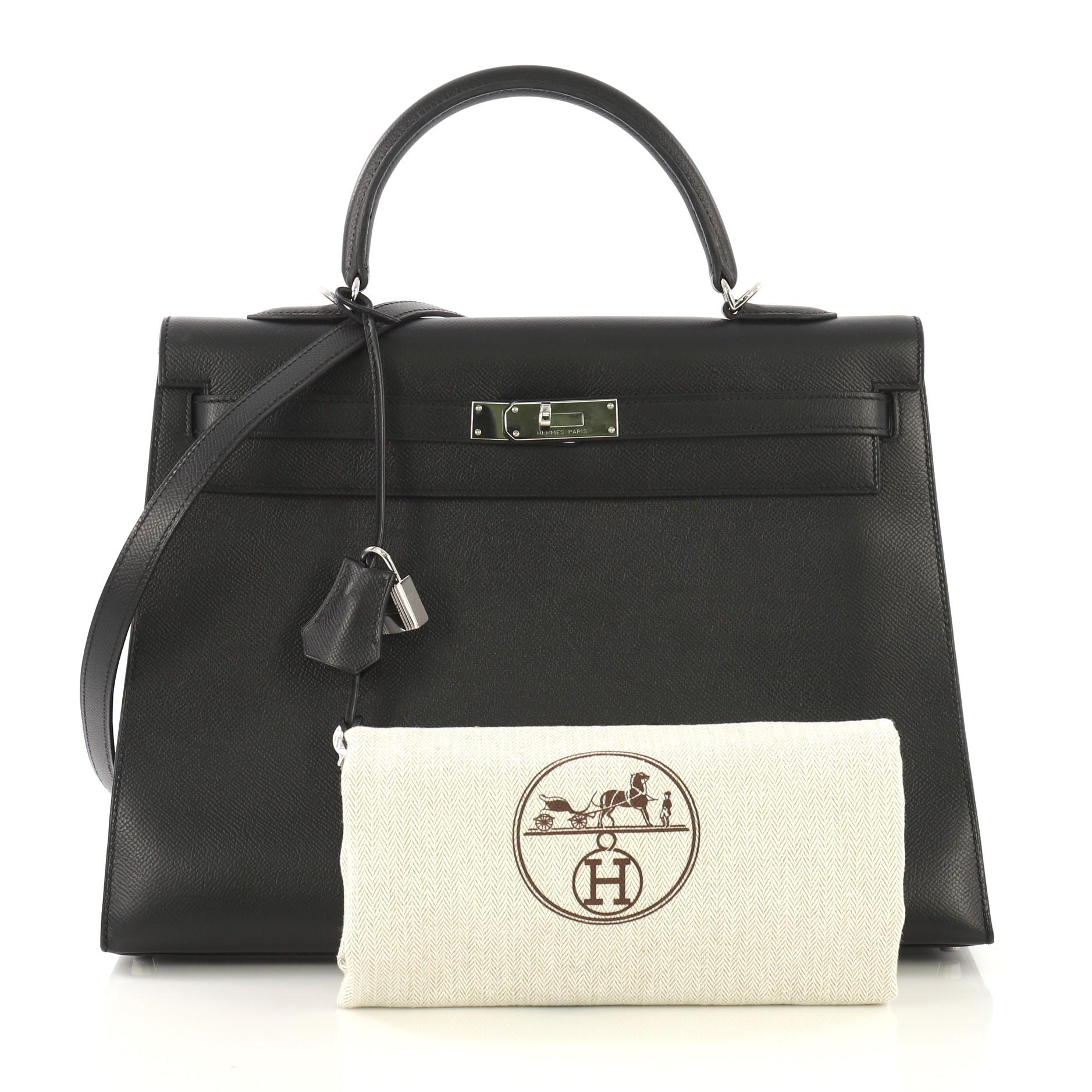 This Hermes Kelly Handbag Noir Epsom with Palladium Hardware 35, crafted in Noir black Epsom leather, features a single rolled top handle, frontal flap, and palladium hardware. Its turn-lock closure opens to a Noir black Chevre leather interior with