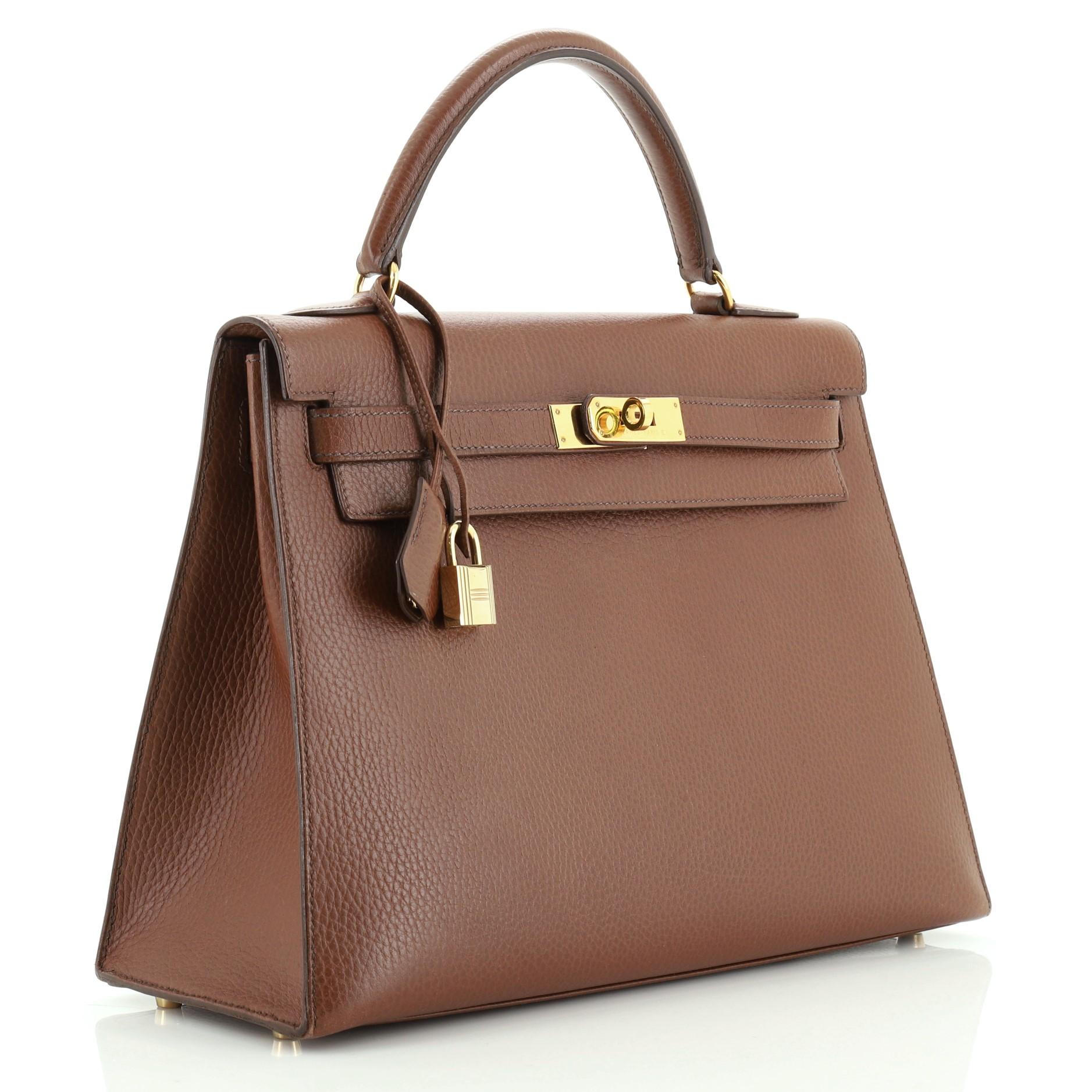This Hermes Kelly Handbag Noisette Ardennes with Gold Hardware 32, crafted in Noisette brown Ardennes leather, features a single top handle, frontal flap, and gold hardware. Its turn-lock closure opens to a Noisette brown Chevre leather interior