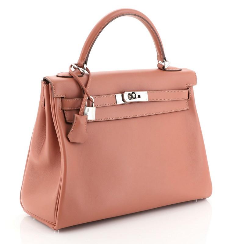 This Hermes Kelly Handbag Rosy Swift with Palladium Hardware 32, crafted from Rosy pink Swift leather, features a single rolled top handle, frontal flap, protective base studs, and palladium hardware. Its turn lock closure opens to a Rosy pink Swift