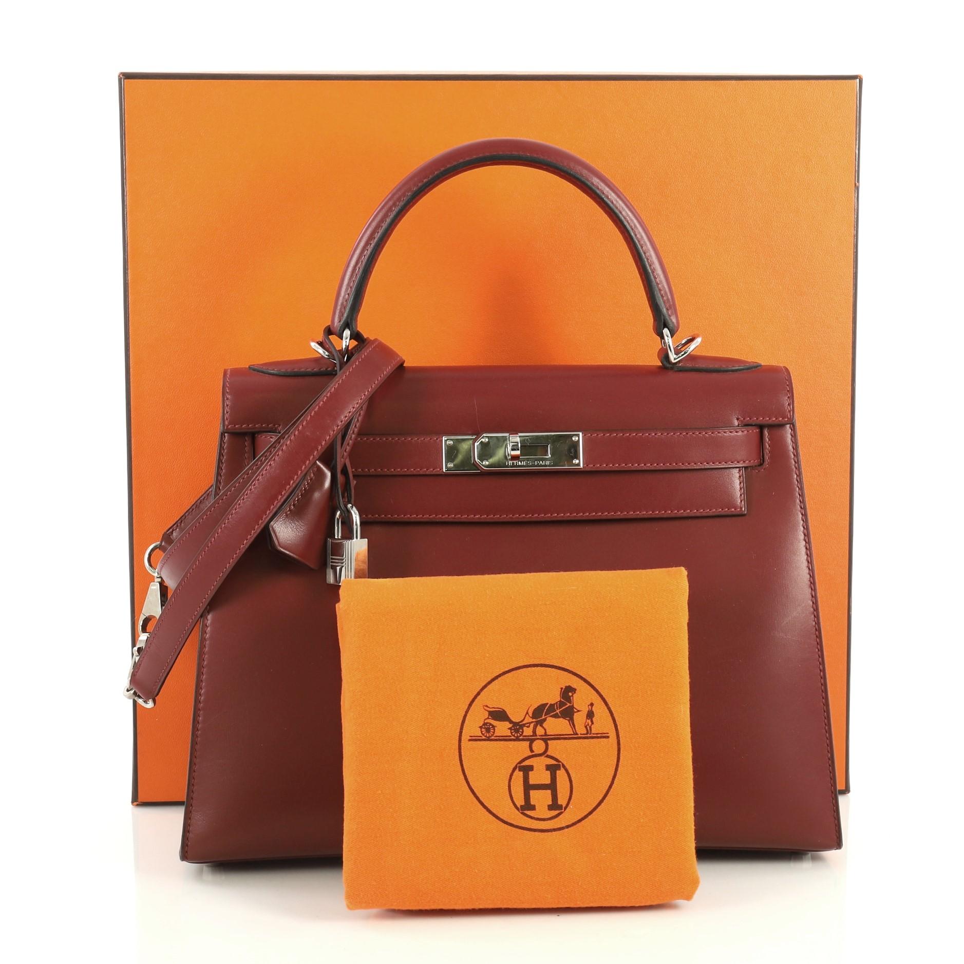 This Hermes Kelly Handbag Rouge H Box Calf with Palladium Hardware 28, crafted in Rouge H red Box Calf leather, features a single rolled top handle, frontal flap, and palladium hardware. Its turn-lock closure opens to a Rouge H red Chevre leather
