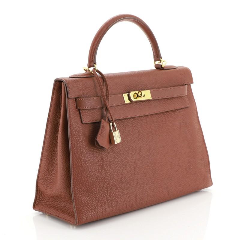 This Hermes Kelly Handbag Sienne Togo with Gold Hardware 32, crafted in Sienne red Togo leather, features a single rolled top handle, frontal flap, and gold hardware. Its turn-lock closure opens to a Sienne red Chevre leather interior with zip and