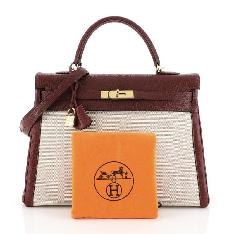 This Hermes Kelly Handbag Toile and Rouge H Chevre de Coromandel with Gold Hardware 35, crafted in Rouge H red Chevre de Coromandel and Ecru neutra Toile H, features a single rolled top handle, protective base studs, and gold hardware. Its turn-lock