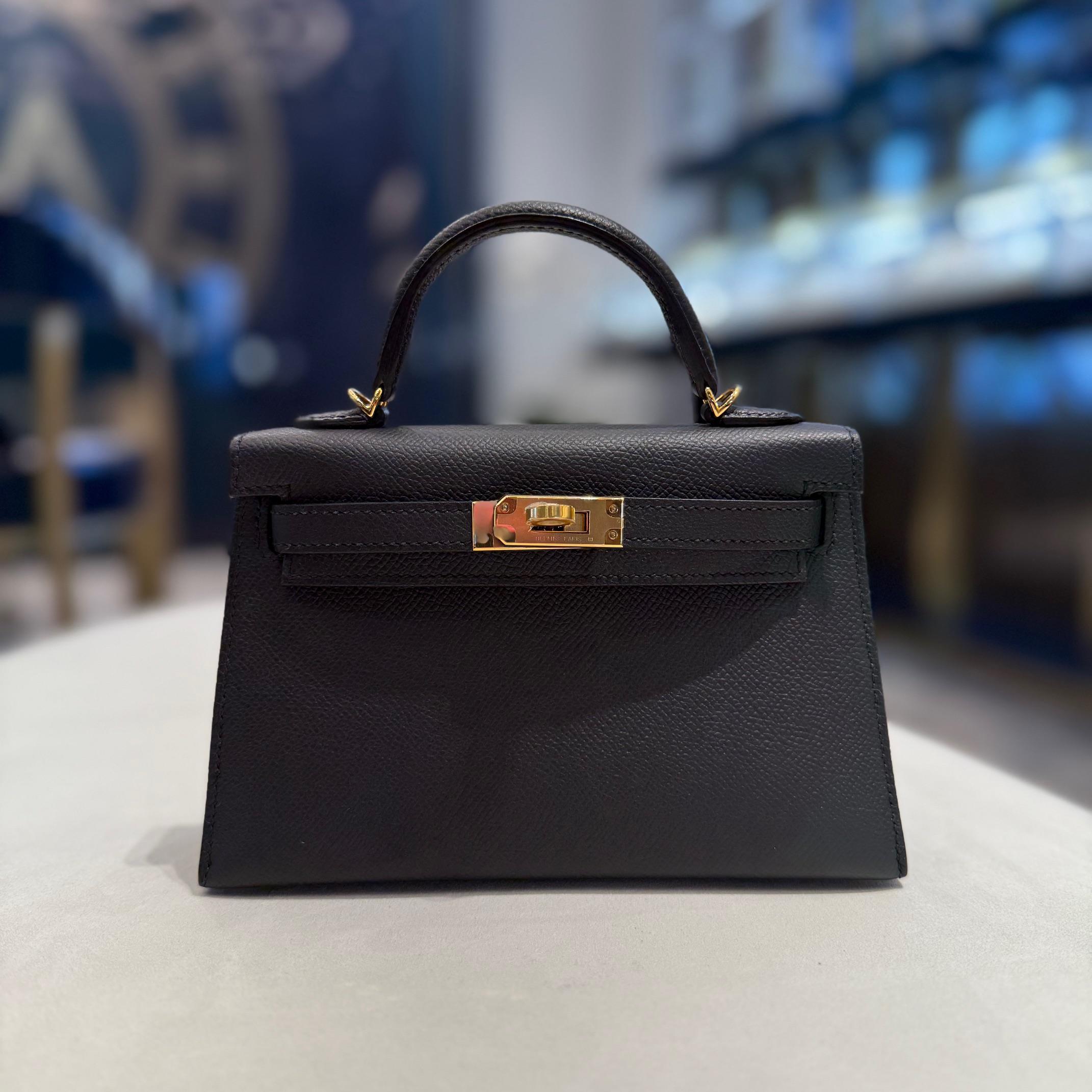Jewels Aficionado offers an Hermès Noir Mini Kelly 20 Sellier in Epsom leather that is a timeless symbol of elegance. Its deep black hue enhances the structured silhouette, while lightweight, scratch-resistant Epsom leather ensures lasting beauty.