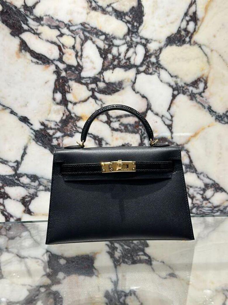 Jewels Aficionado offers The Hermès Noir Mini Kelly 20 Sellier in Touch Veau Madame and Lezard combines timeless elegance with exotic luxury. The deep black Noir color complements the structured silhouette, while the mix of smooth Veau Madame and