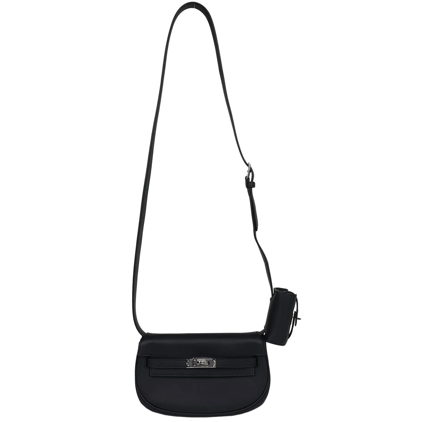 This Kelly Moove Black swift calfskin leather with palladium hardware features tonal stitching, a round half-moon shape, pull straps attached to a toggle closure, and an adjustable flat leather strap with a small pouch. The interior is lined in