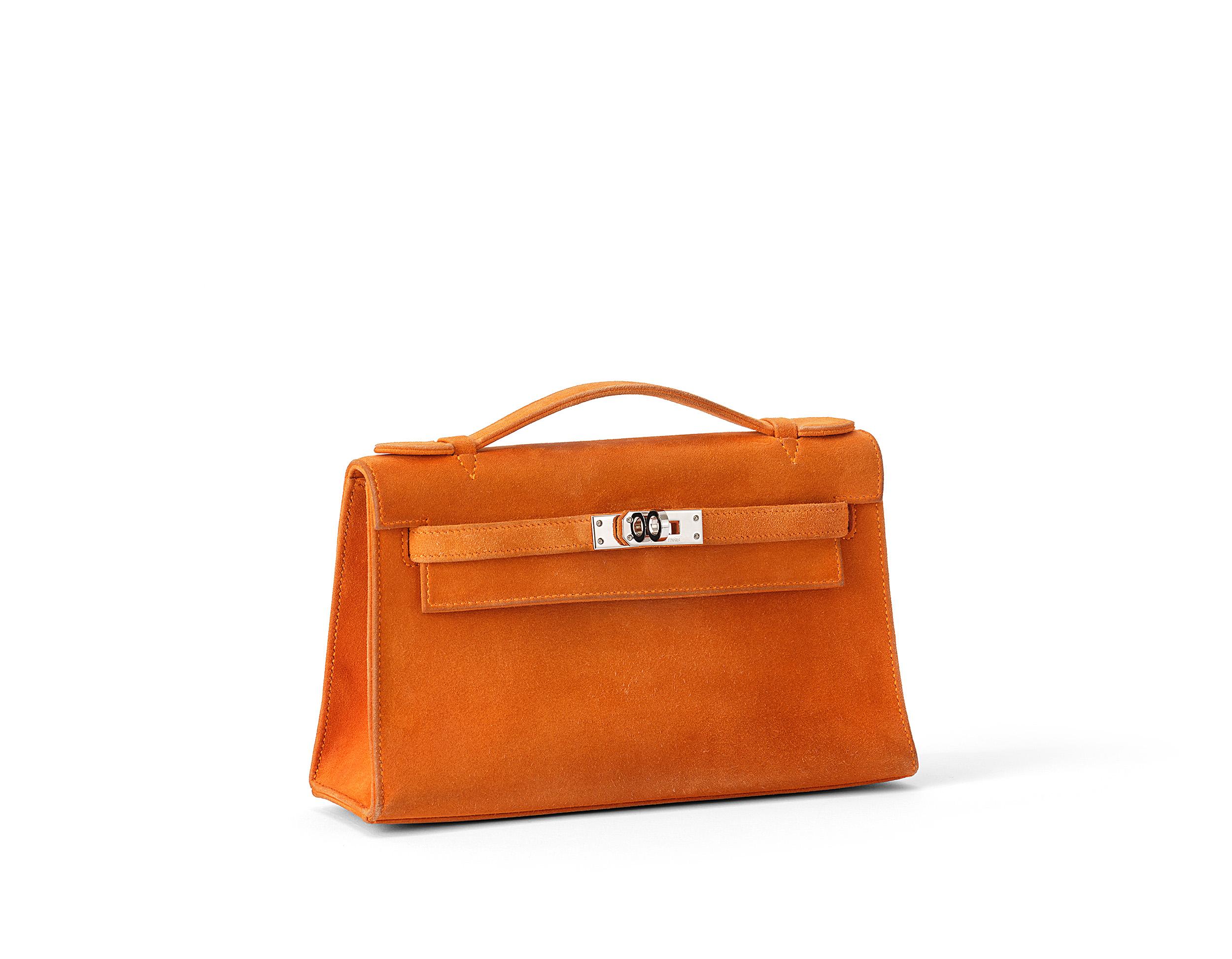 Hermès Kelly Pochette in orange and doblis leather with palladium hardware. The bag is in good used condition. It shows some signs of wear, especially on the corners. There are pen marks inside the bag and scratches on the hardware. The bag was in