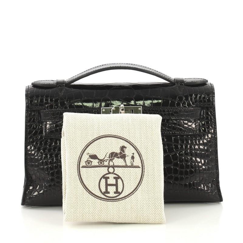 This Hermes Kelly Pochette Shiny Alligator, crafted in genuine Noir black Shiny Alligator, features a frontal flap, top flat handle and palladium hardware. Its turn-lock closure opens to a Noir black Agneau leather interior. Date stamp reads: X