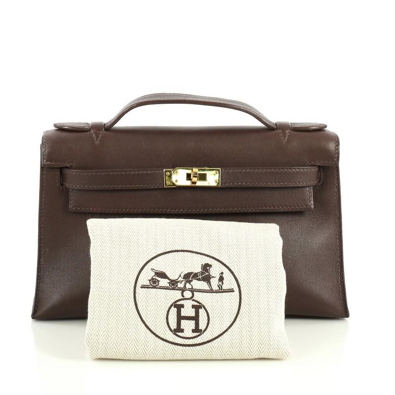 This Hermes Kelly Pochette Swift, crafted in Chocolate brown Swift leather, features top flat handle, frontal flap, and gold hardware. Its turn-lock closure opens to a Chocolate brown Swift leather interior with slip pocket. Date stamp reads: K