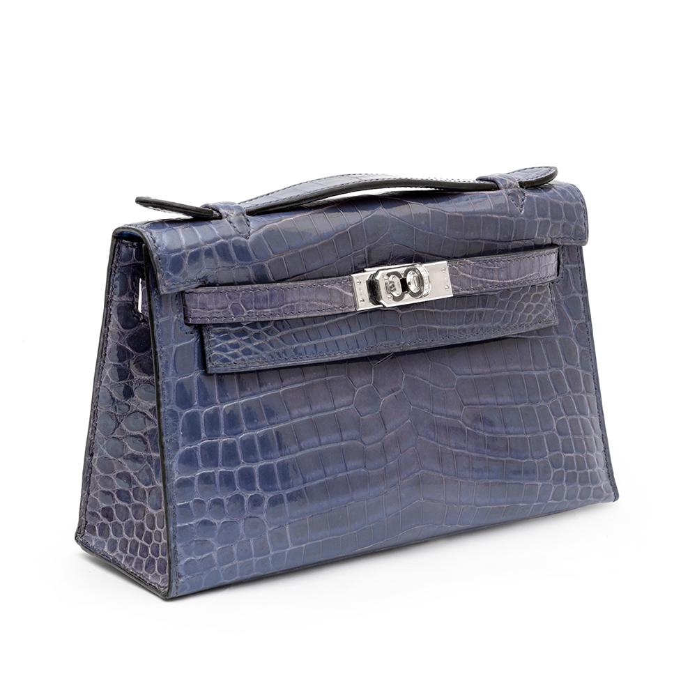 Inspired by Hermès' Kelly tote bag, designed with the iconic details of it's big sister and meticulously crafted from a shiny, rich and opulent Brighton Blue Crocodile leather, this miniature Hermès Kelly Pochette clutch bag is sure to make a