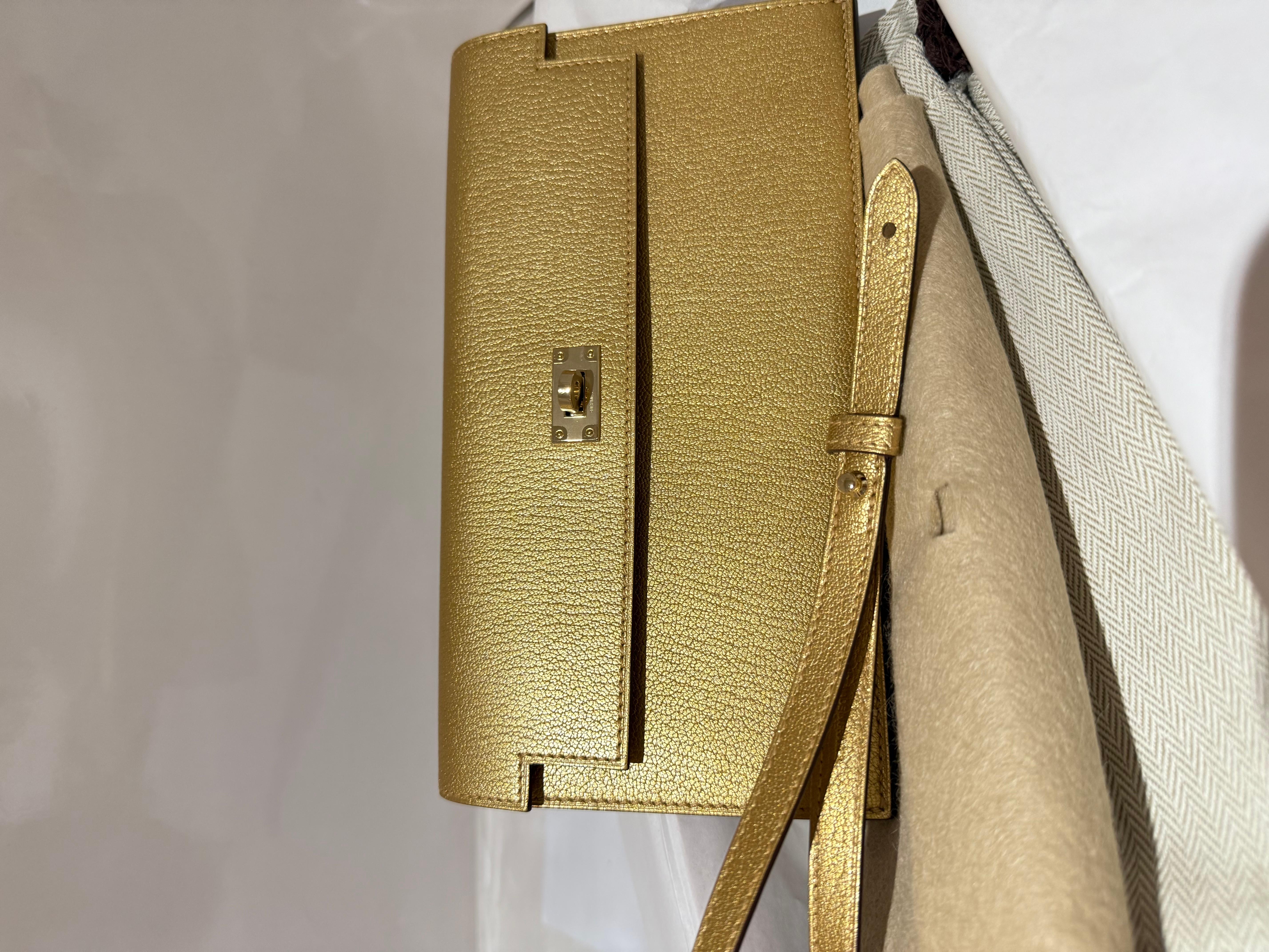 Hermes Kelly Pocket Portefeuille long avec poignée en couleur or. Ce portefeuille long en peau de chèvre Chamkilight de couleur Doré (or) avec des ferrures dorées. Il dispose de 4 fentes pour cartes de crédit et d'une pochette zippée. Livré avec