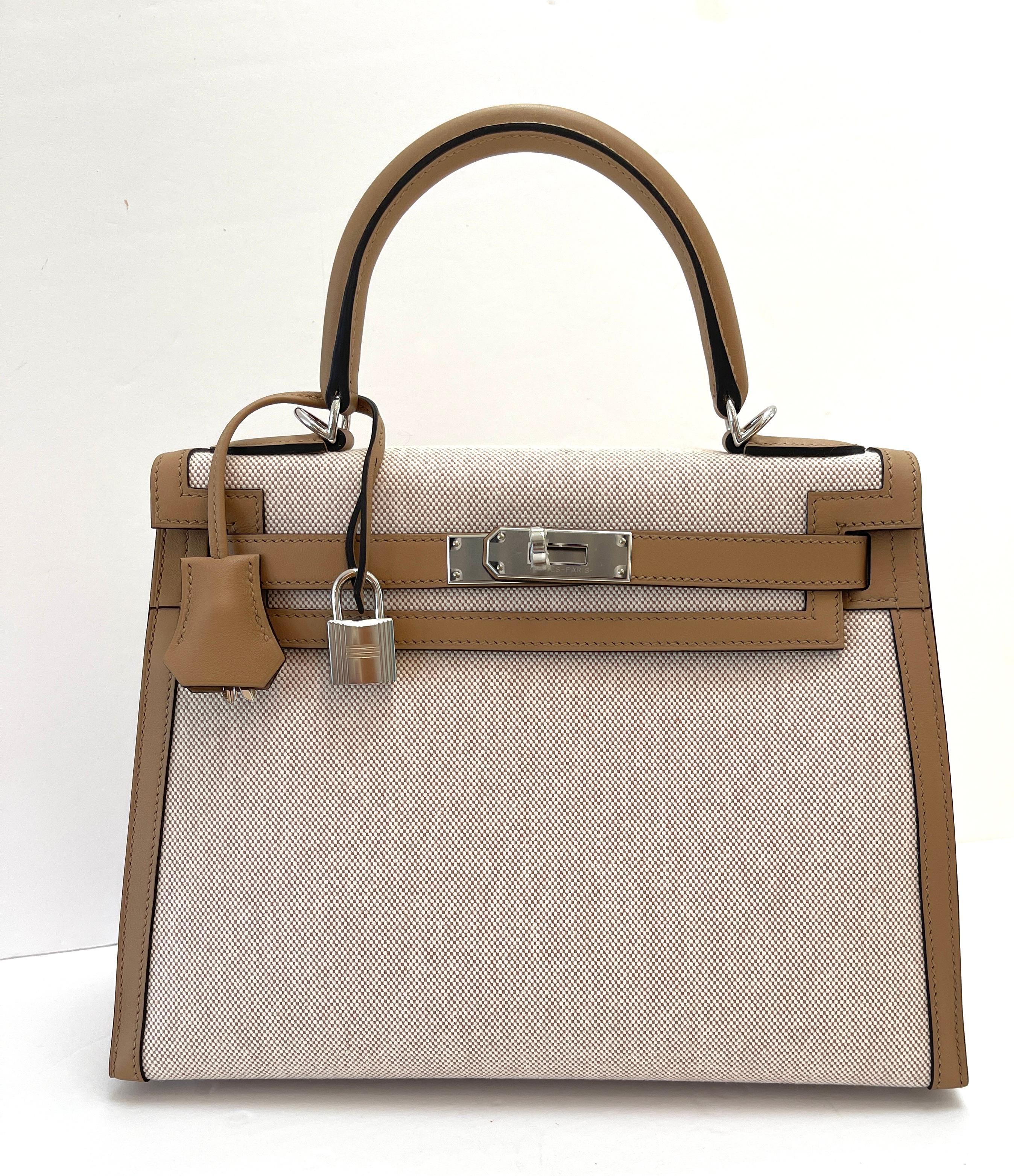 This Sellier Kelly is of Chai toile and swift leather with palladium hardware and features tonal stitching, front flap, two straps with center toggle closure, clochette with lock and two keys, single rolled handle and removable leather shoulder