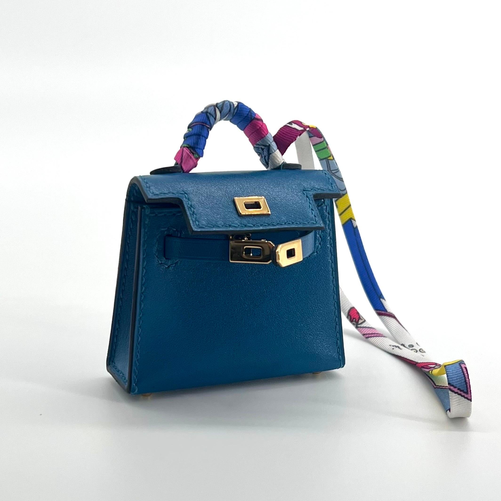 This Micro Mini Kelly Twilly bag charm from Hermès is the smallest Mini Kelly bag. This Hermès Kelly Twilly Charm is made from Veau Tadelakt leather with a Gold Hardware. Similar to swift leather. The beautiful charm is in the colour of Bleu Izmir