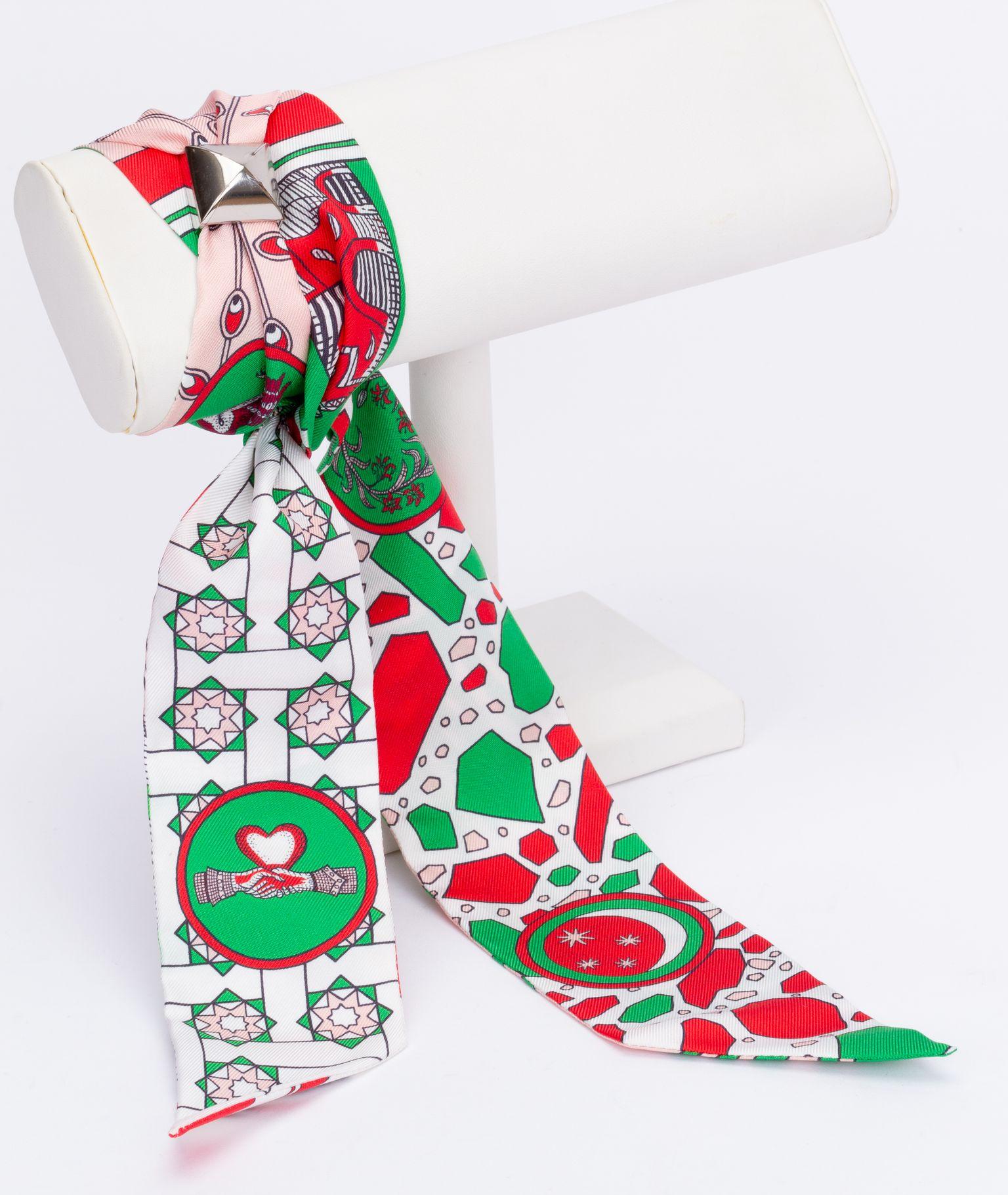 New Hermès La Danse Des Amazones Twilly. The scarf is made out of silk and the main color is pink and green. The print shows animals like an owl. The piece comes with a scarf ring, original box and ribbon.