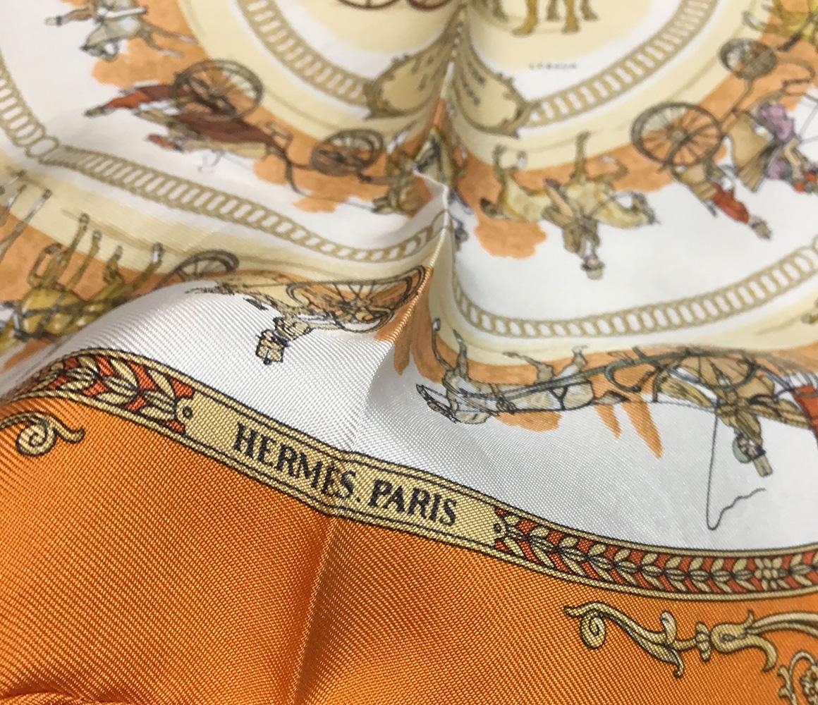 Hermes La Promenade de Longchamps Pocket Square Scarf in Orange. Original silk screen design c1965 by Philippe Ledoux features an array of horse drawn carriages in a circle pattern over a cream background surrounded by an orange border. 100% silk,