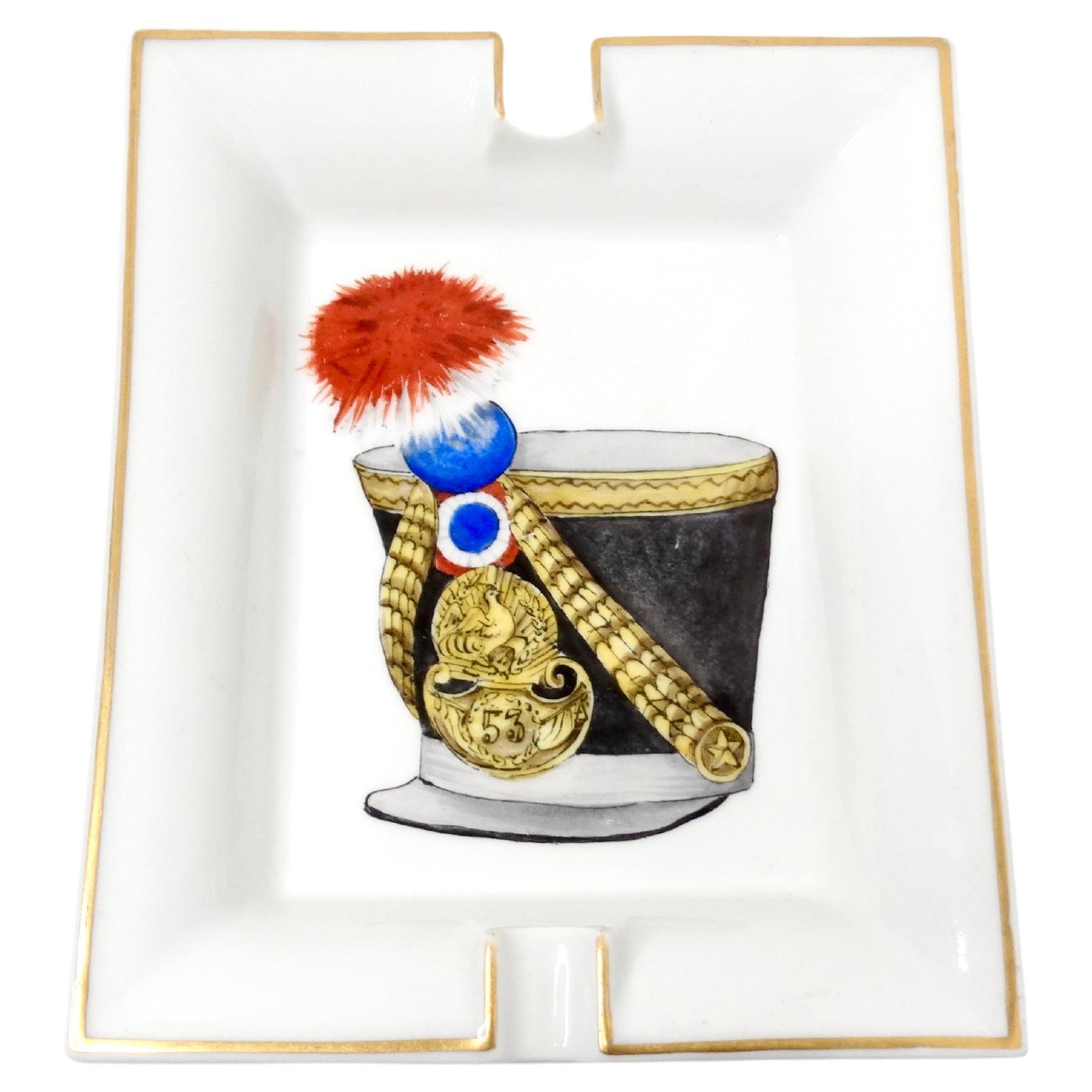 Der Hermes Large Porcelain French Military Hat Motif Ashtray ist ein luxuriöses und unverwechselbares Dekorationsstück, das Eleganz mit historischem Charme verbindet. Dieser aus feinem Porzellan gefertigte Aschenbecher zeigt ein detailliertes und