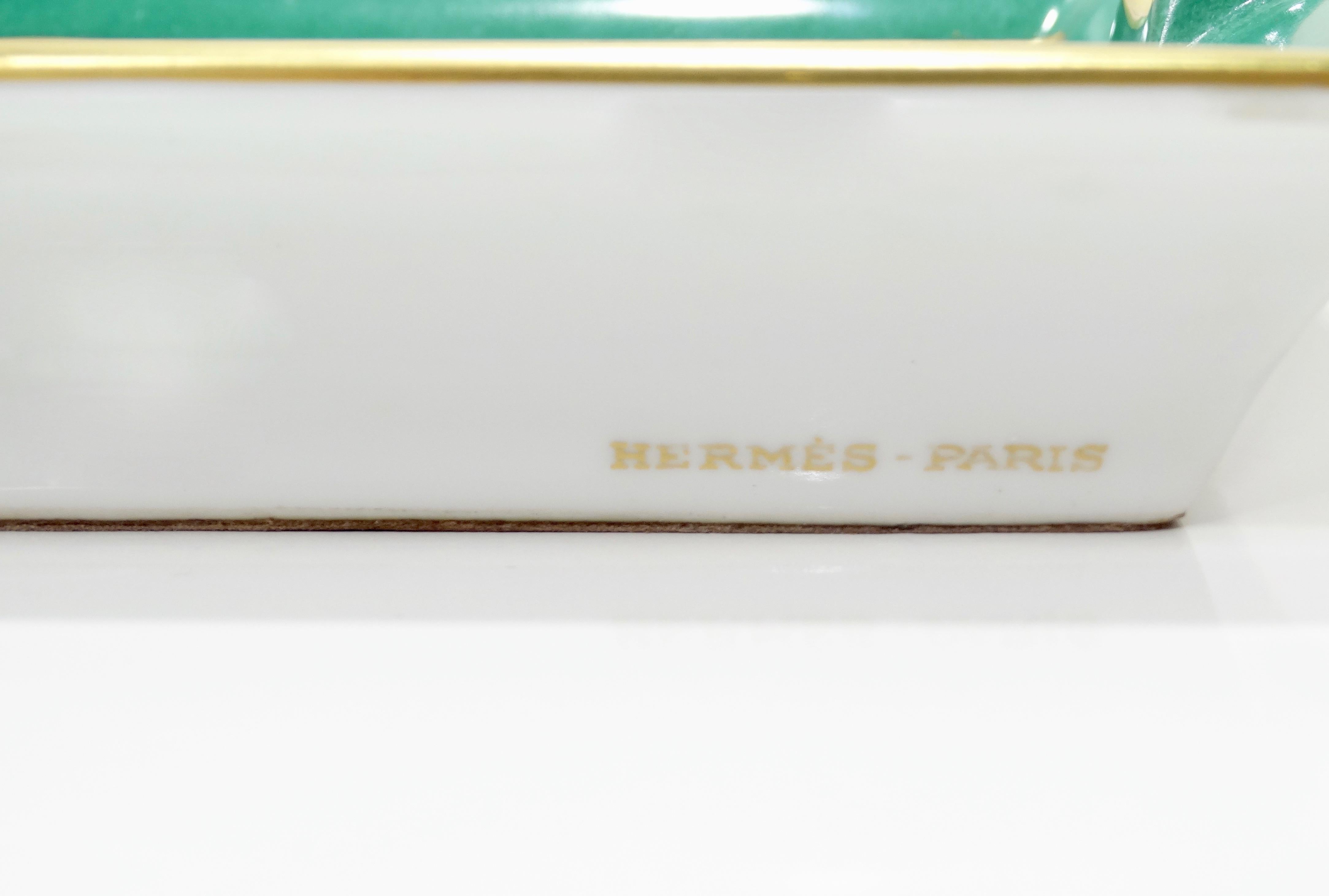 Decorate in style with this amazing Hermés tray! Circa late 20th century, this tray is crafted from porcelain and features a motif of three decorated cheval horses (two white and one emerald green). Trim is painted in metallic gold and tonal emerald