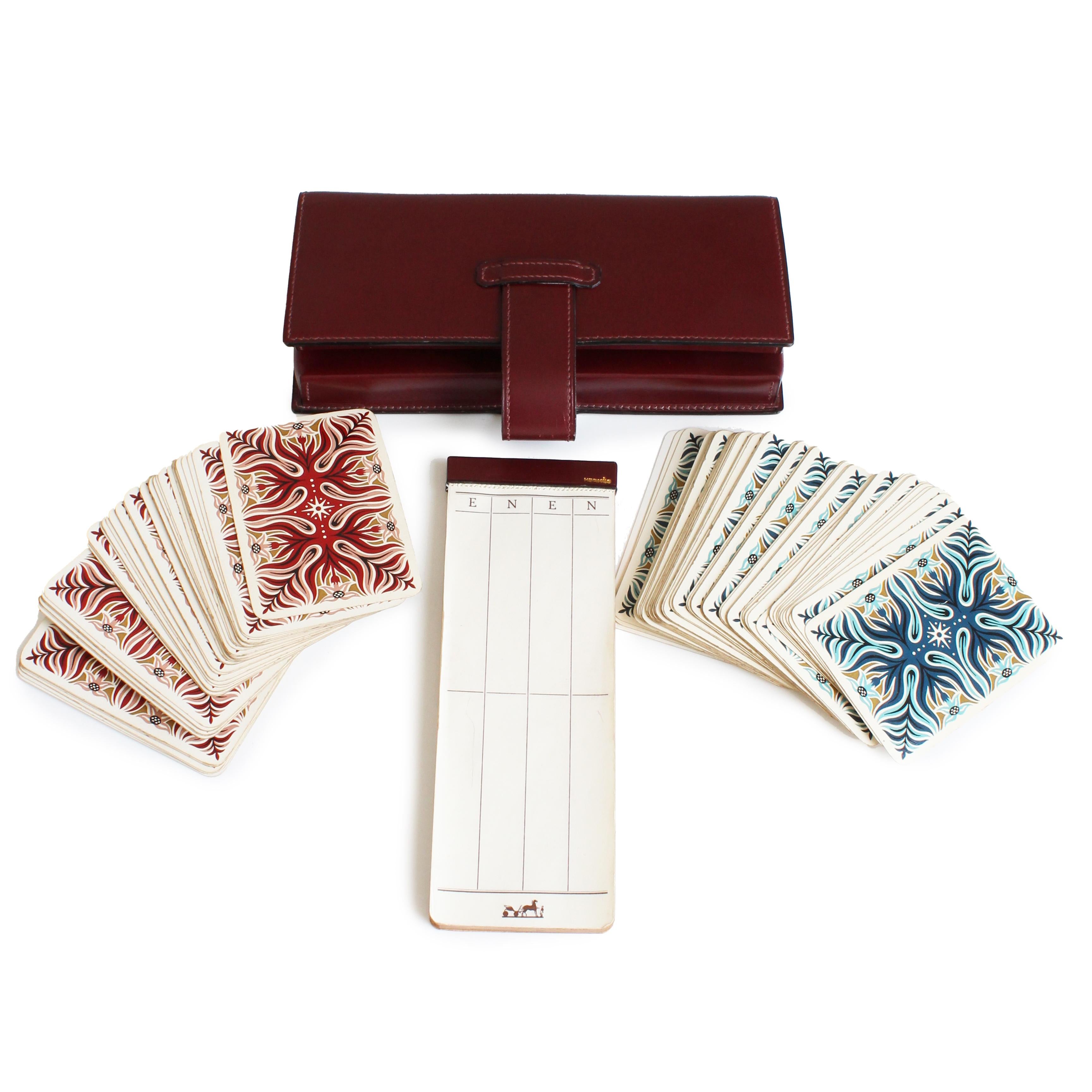Preowned, vintage Hermes leather card game case with score card and playing cards designed by AM Cassandre, likely made in the late 70s, early 80s.  Made from a burgundy-hued box leather, it fastens with a leather tab and opens to reveal a two-set