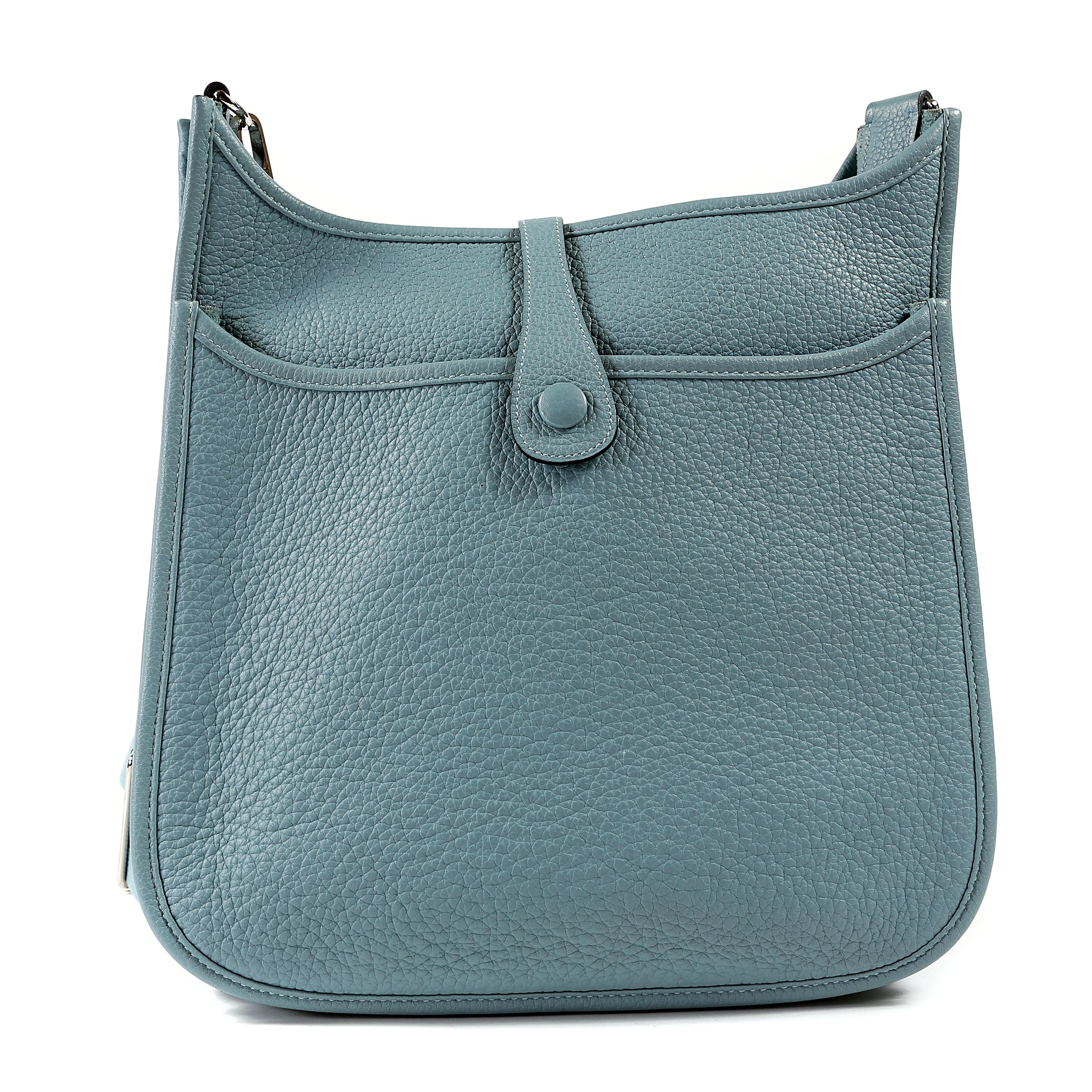 This authentic Hermès Light Blue Clemence Medium Evelyne PM III is in pristine condition. Extremely sought after, the Evelyne is an understated day bag that is stylish and practical.  The third generation sports a rear pocket and adjustable canvas