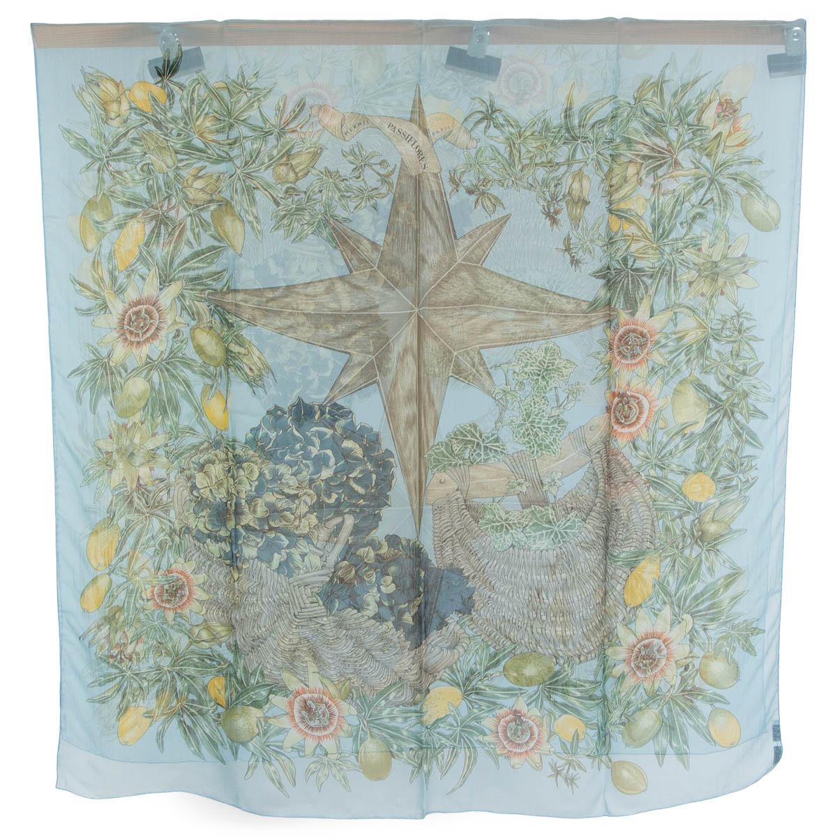 100% authentic Hermès Passiflores oblong mousseline shawl in light blue silk chiffon (100%) an elaborate design of florals and fruits on a background of light blue with details in taupe, green, navy blue, yellow and orange. Has been worn and is in