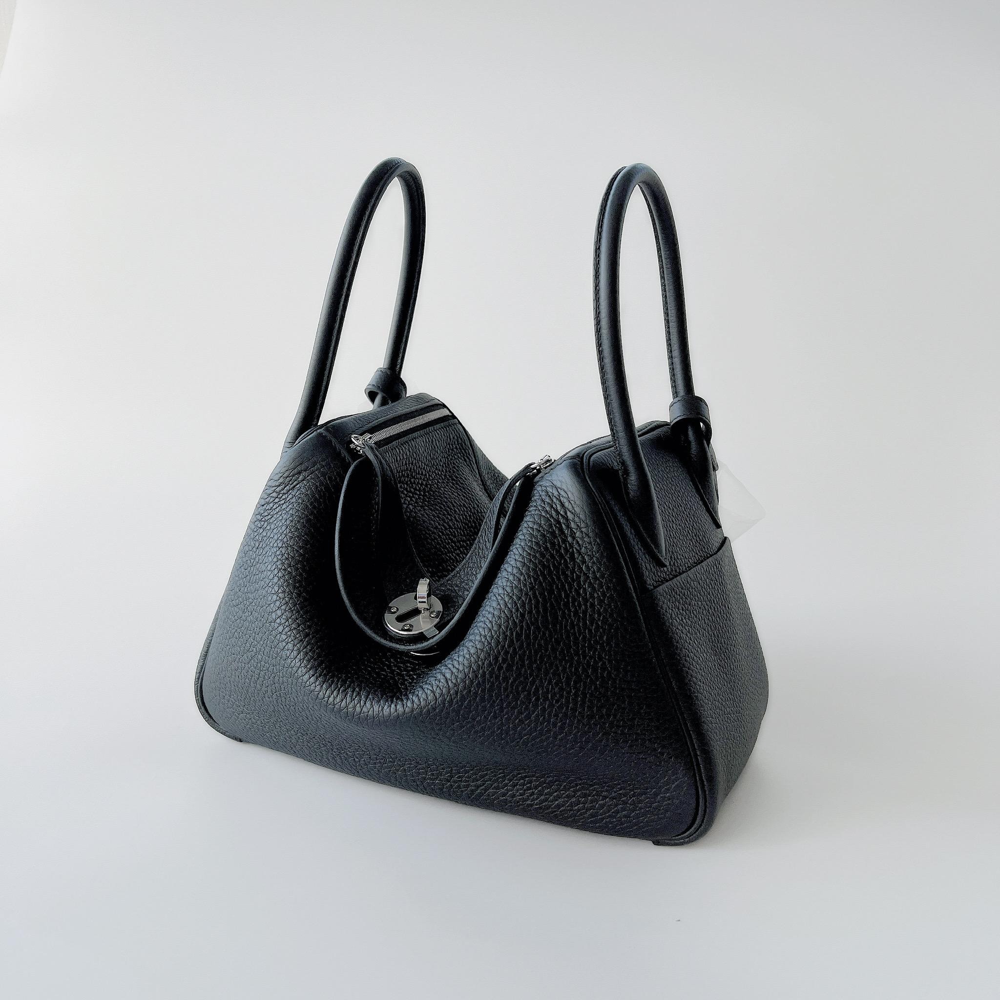 Shop this classic coloured Hermes Lindy 26 In Black Clemence Leather. It features Palladium Hardware which gives the bag a more younger and stylish look. The Lindy 26 is a fantastic size bag for everyday use and fits much more than the Mini Lindy.