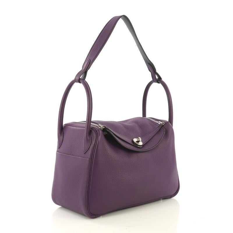 This Hermes Lindy Eclat Handbag Clemence 30, crafted from Ultraviolet purple clemence leather, features dual rolled handles, exterior side slip pockets, protective base studs, and palladium hardware. Its turn-lock and zip closure opens to a Bleu