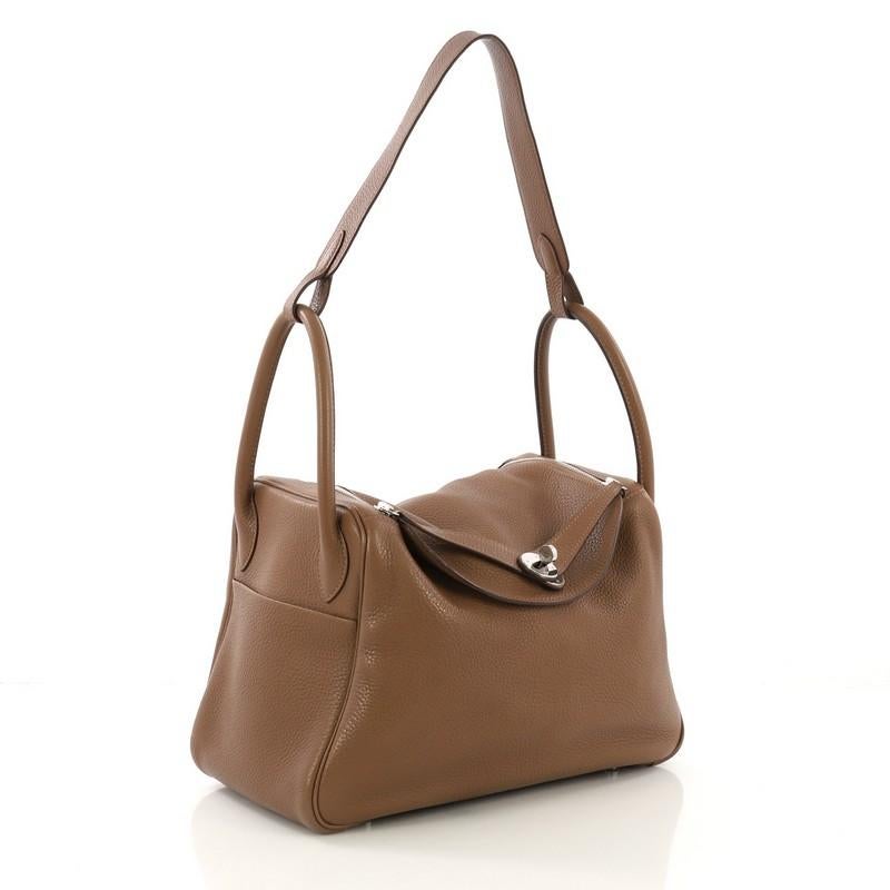 This Hermes Lindy Handbag Clemence 30, crafted from Alezan brown Clemence leather, features dual rolled handles, two side slip pockets, and palladium hardware. Its turn-lock and dual zip closure opens to an Alezan brown Chevre leather interior. Date