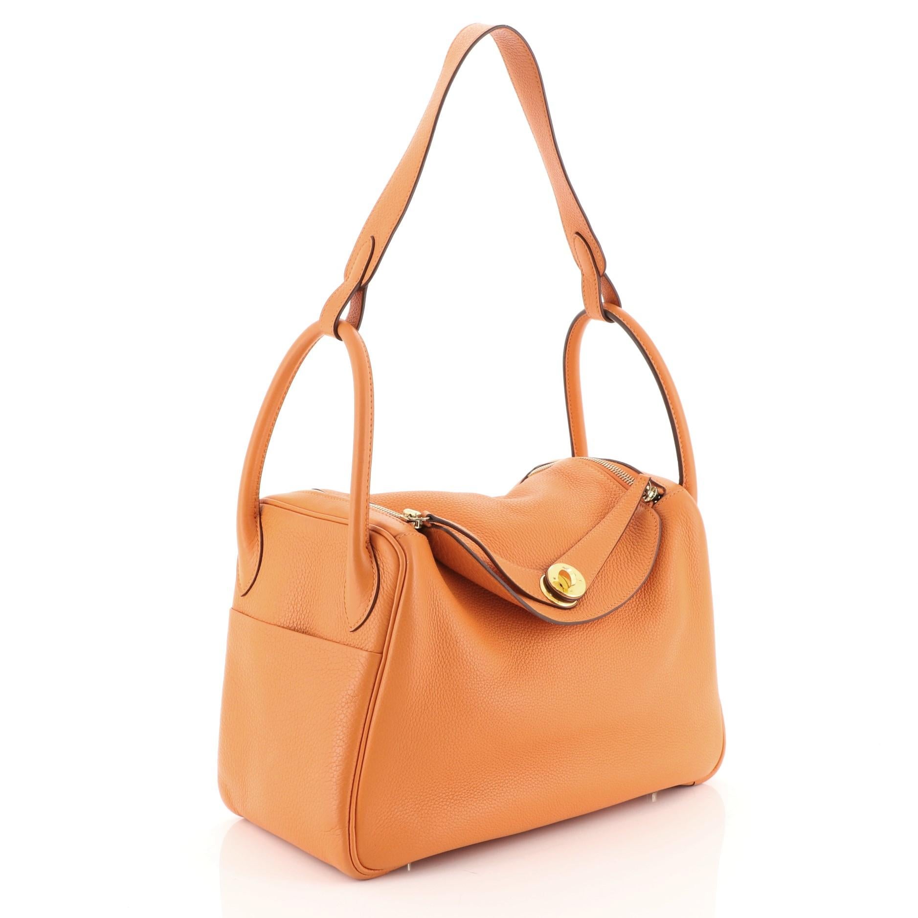 This Hermes Lindy Handbag Clemence 30, crafted in Orange H orange Clemence leather, features dual-rolled handles, two sides slip pockets, a connecting long strap and gold hardware. Its turn-lock and top-zipper closure opens to an Orange H orange